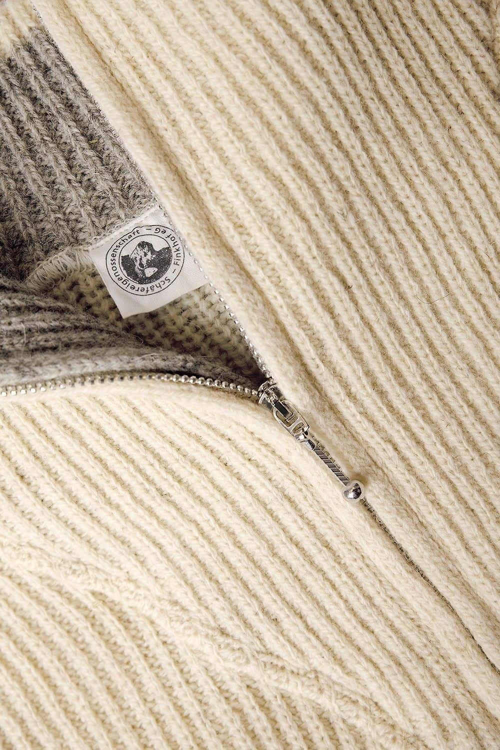 Detailaufnahme vom Reißverschluss und Etikett des naturweißen Finkhof Troyer aus bio Wolle (kbA)