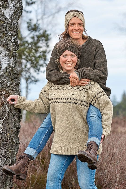 Frauen heben sich Huckepack und tragen Stirnbänder und Finkhof Norwegerpulli aus bio Wolle (kbT)