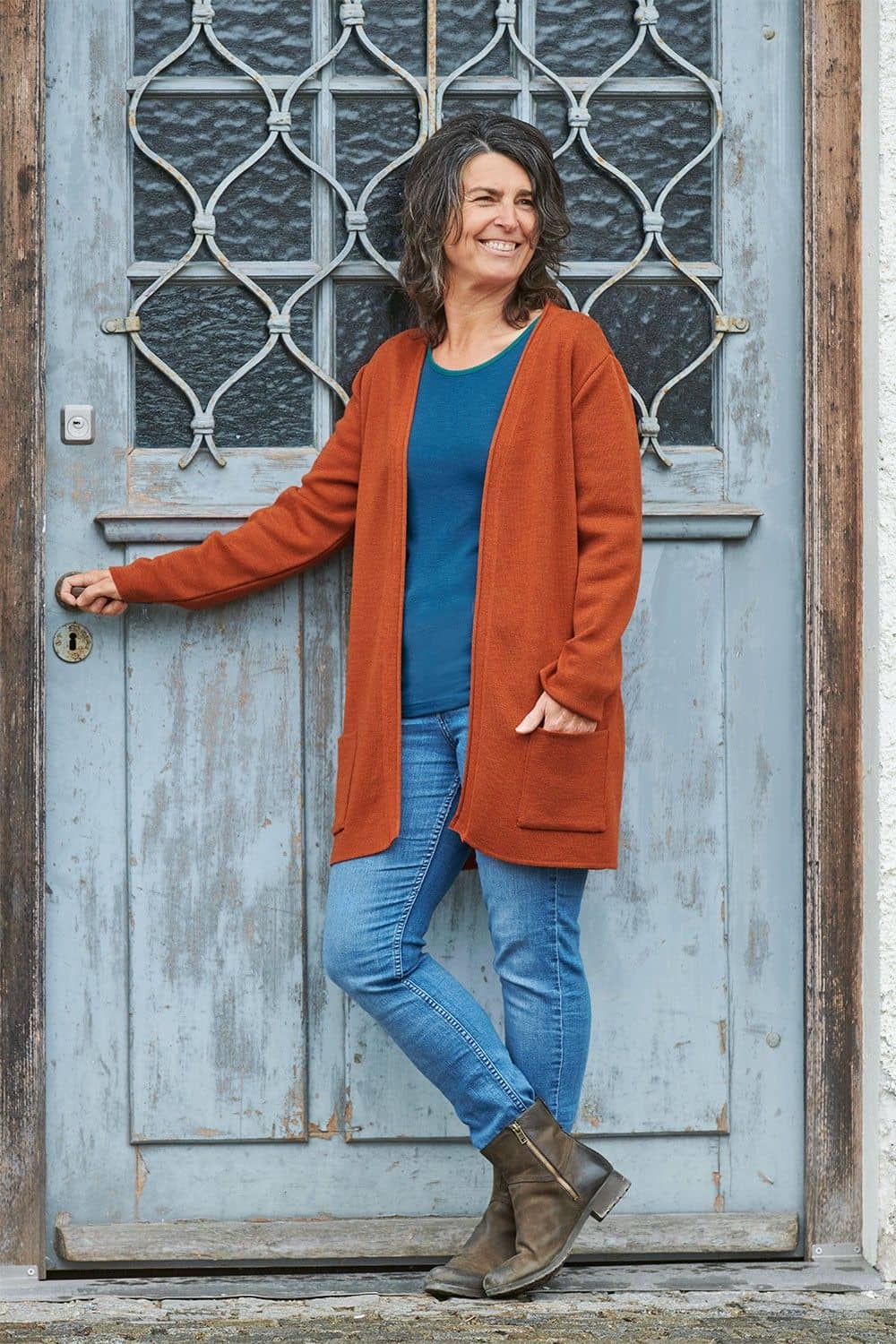 Frau mit blauem Shirt und Jeans trägt orangen langen Cardigan aus bio Merinowolle (kbT)