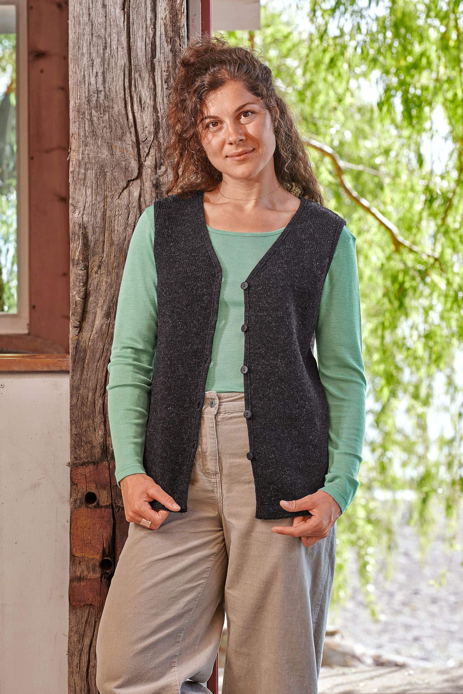 Finkhof-Strickweste fein Frau trägt eine graue Strickweste ohne Ärmel aus bio Wolle (kbT) vom Finkhof mit grünem Shirt und beiger Hose