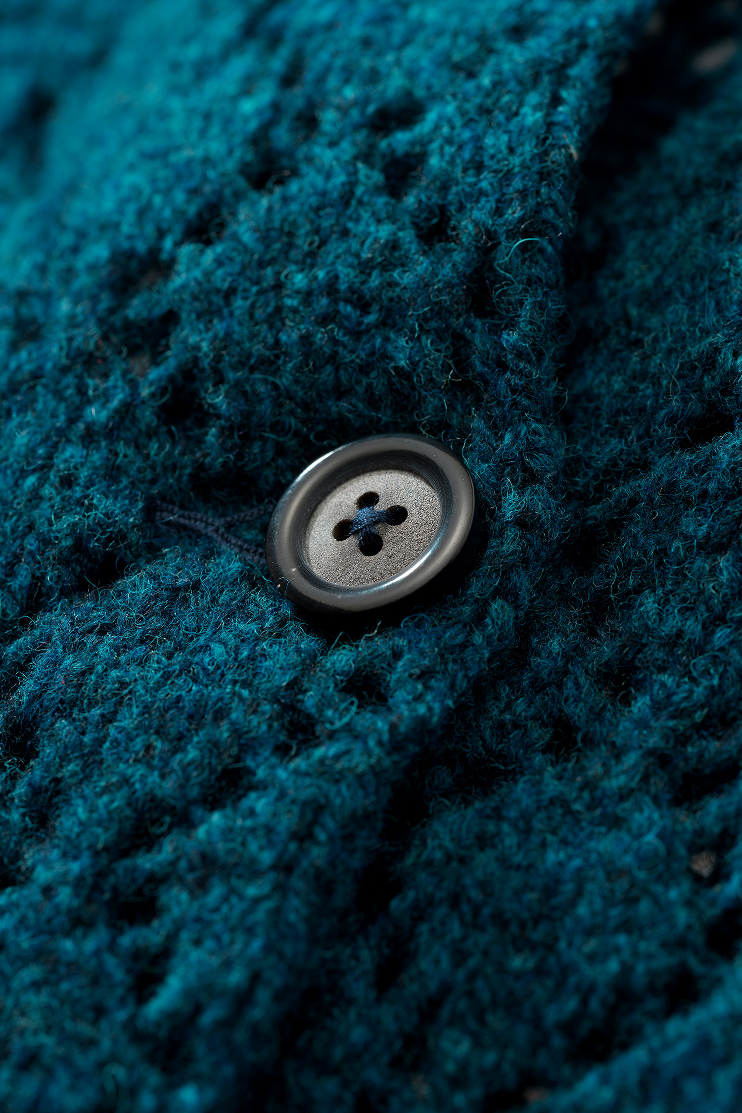 Nahaufnahme der Struktur und eines Knopfes der blauen Damenstrickjacke mit Ajourmuster aus Bio-Wolle vom Finkhof