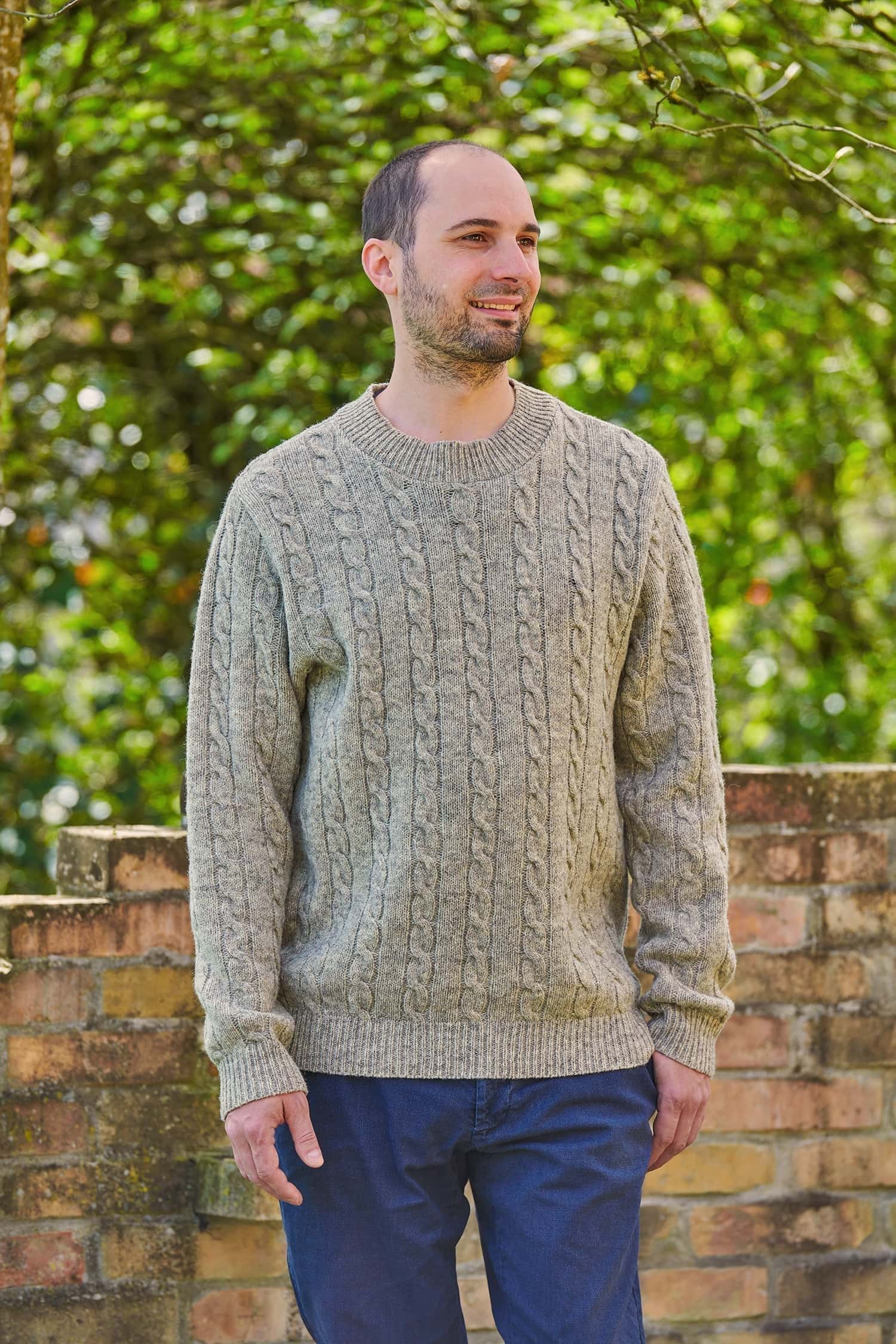 Mann trägt grauen Wollpullover vom Finkhof mit Zopfstrickmuster aus Bio-Wolle und dazu eine Jeans