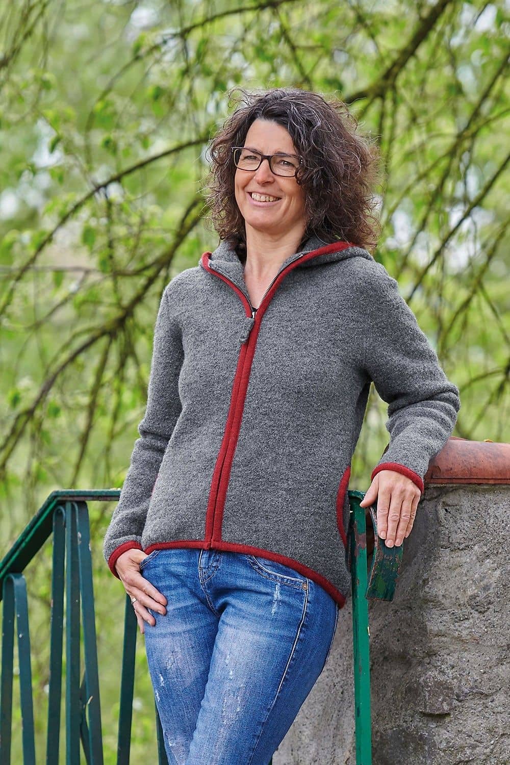 Jacke Reni grau Gr. S Frau lehnt sich an Geländer und trägt eine graue Strickwalk Jacke aus bio Wolle (kbT) vom Finkhof