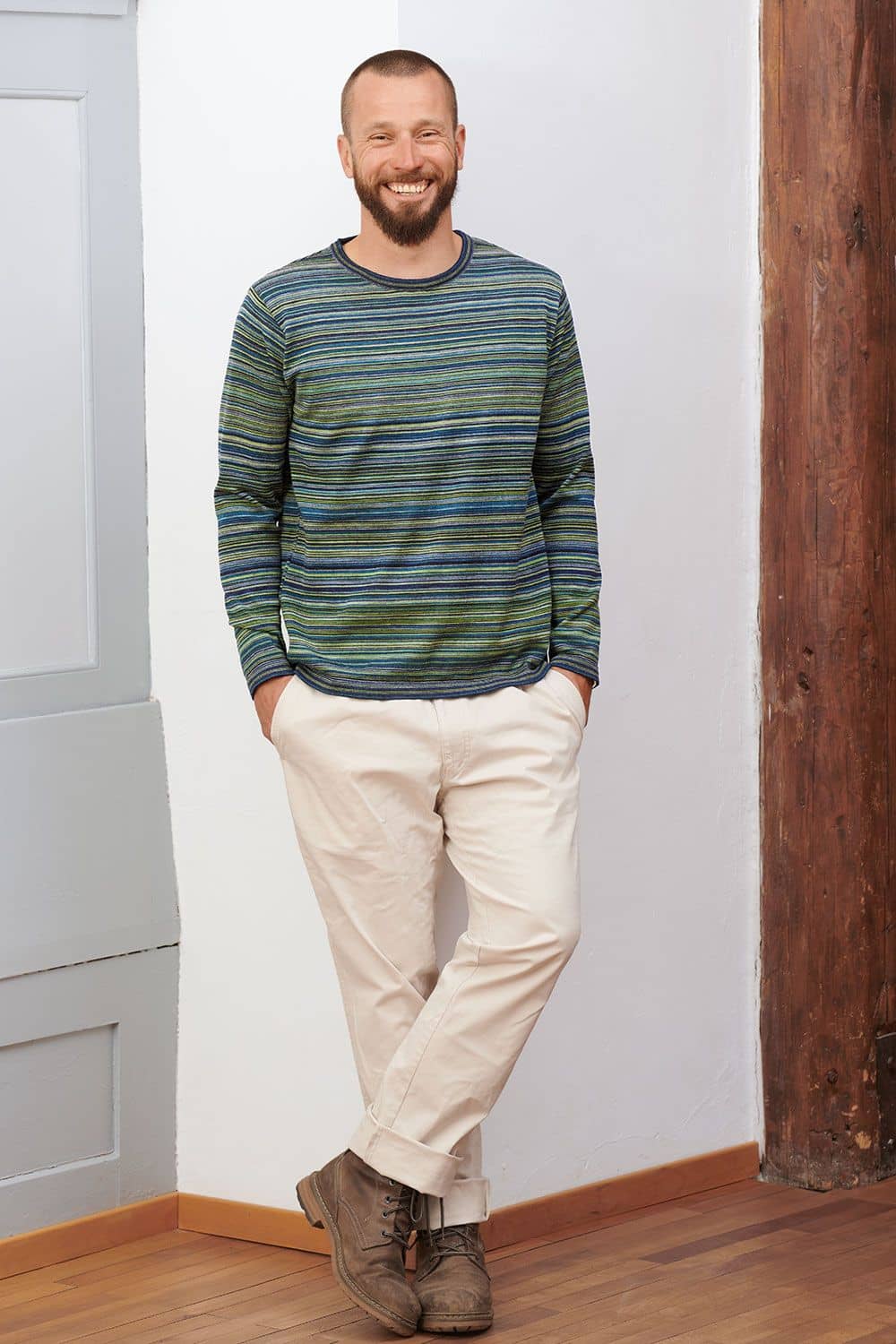 Herrenshirt Feinringel lachender Mann mit beiger Jeans lehnt an Wand und trägt blau grün gestreiftes Shirt aus bio Wolle (kbT) vom Finkhof