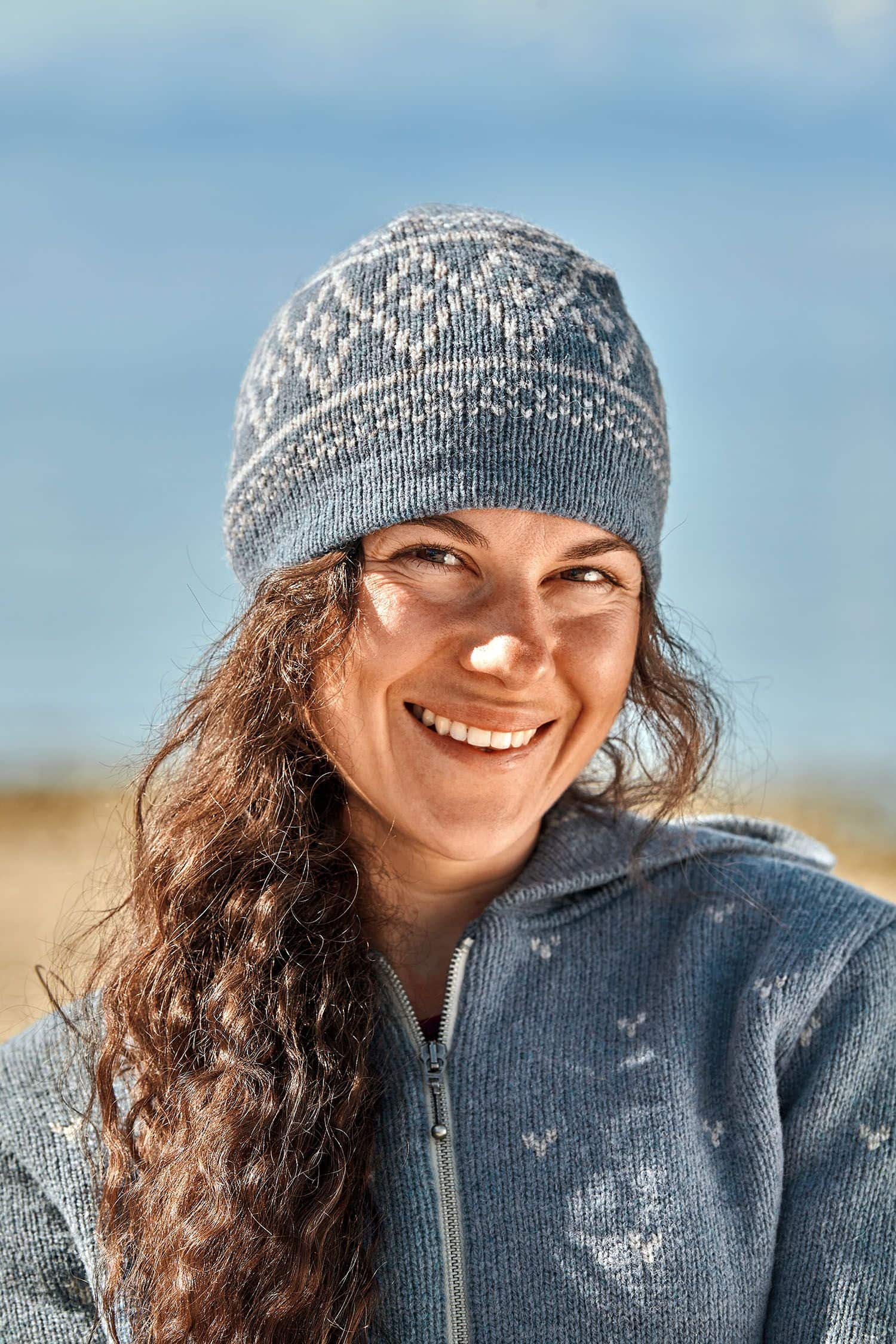 Finkhof-Norweger-Mütze rauchblau Frau trägt rauchblaue Mütze mit Norwegermuster aus bio Wolle (kbT) vom Finkhof und eine blaue Jacke