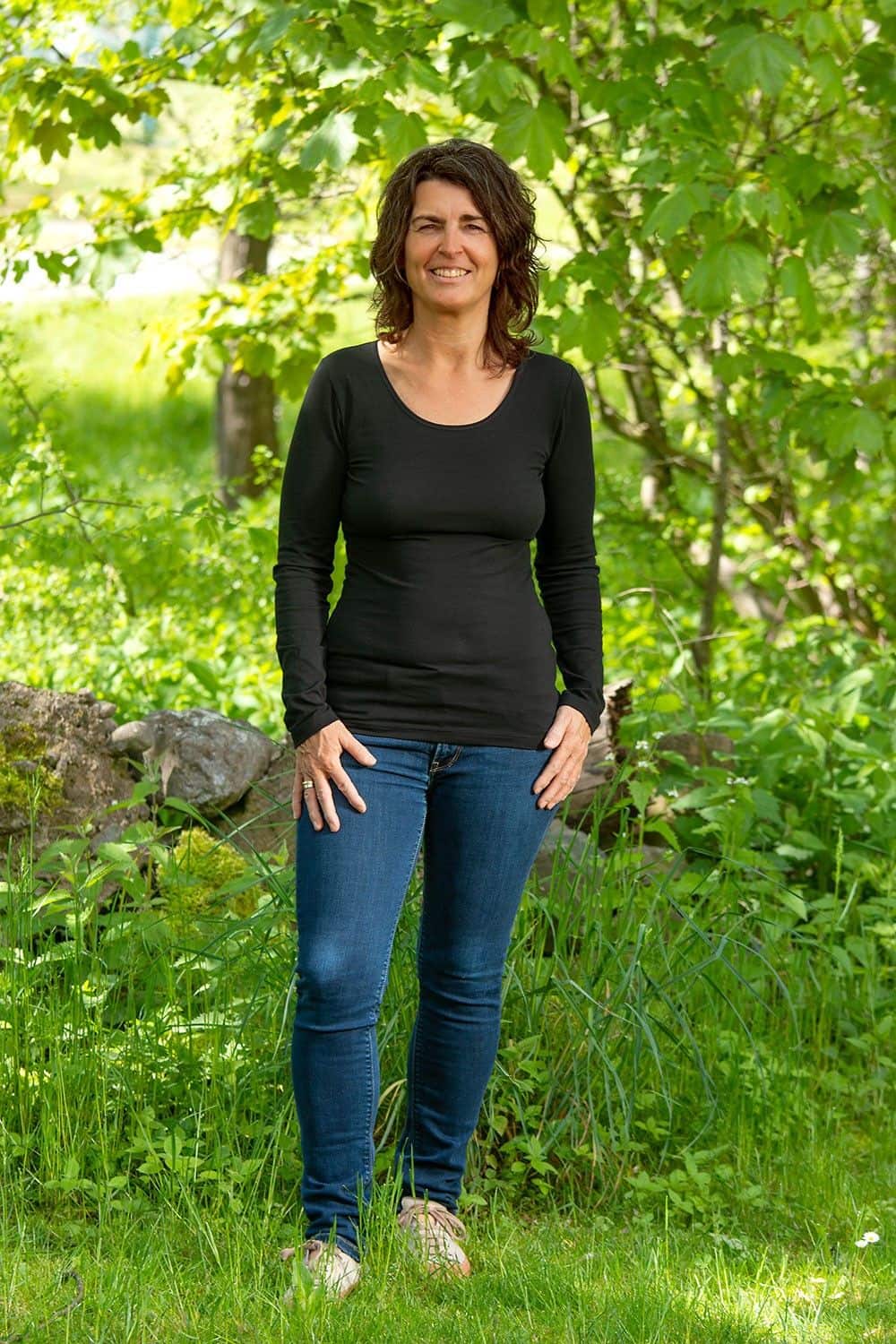 Baumwoll-Langarmshirt schwarz Gr. 38 Frau steht im Grünen und trägt eine Jeans mit schwarzem Langarmshirt aus bio Baumwolle (kbA) und Elasthan