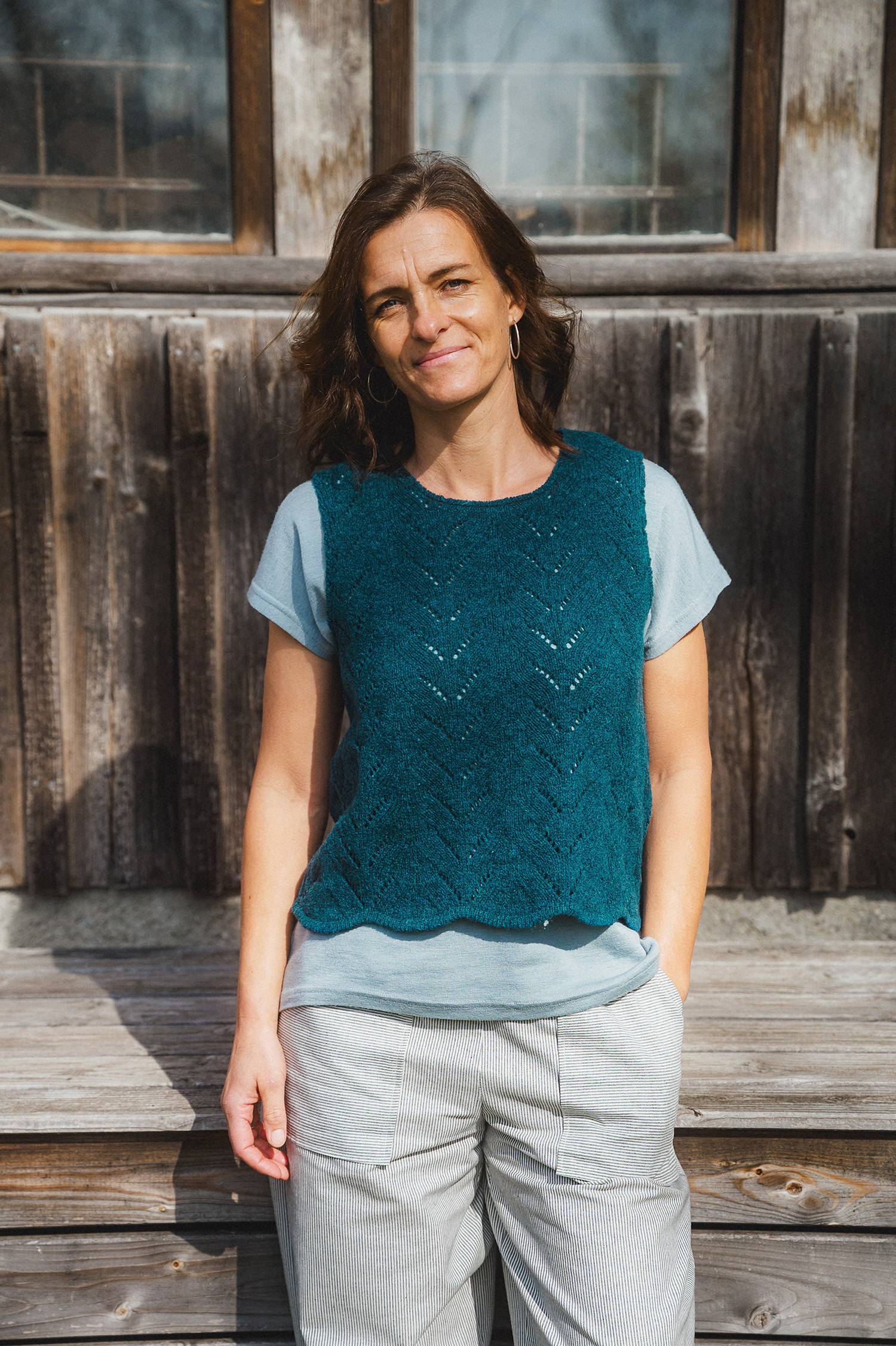 Finkhof-Ajour-Damen-Strickpullunder aus reiner Bio-Schurwolle Frau trägt blaues Langarmshirt und helle Baumwollhose mit blauem Strickpullunder aus Bio-Wolle vom Finkhof