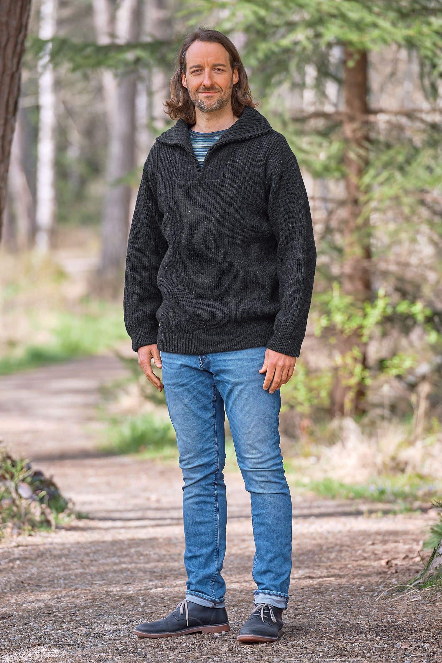 Mann mit Jeans trägt anthraziten Finkhof Troyer mit Zipper aus bio Wolle (kbT) und steht im Wald