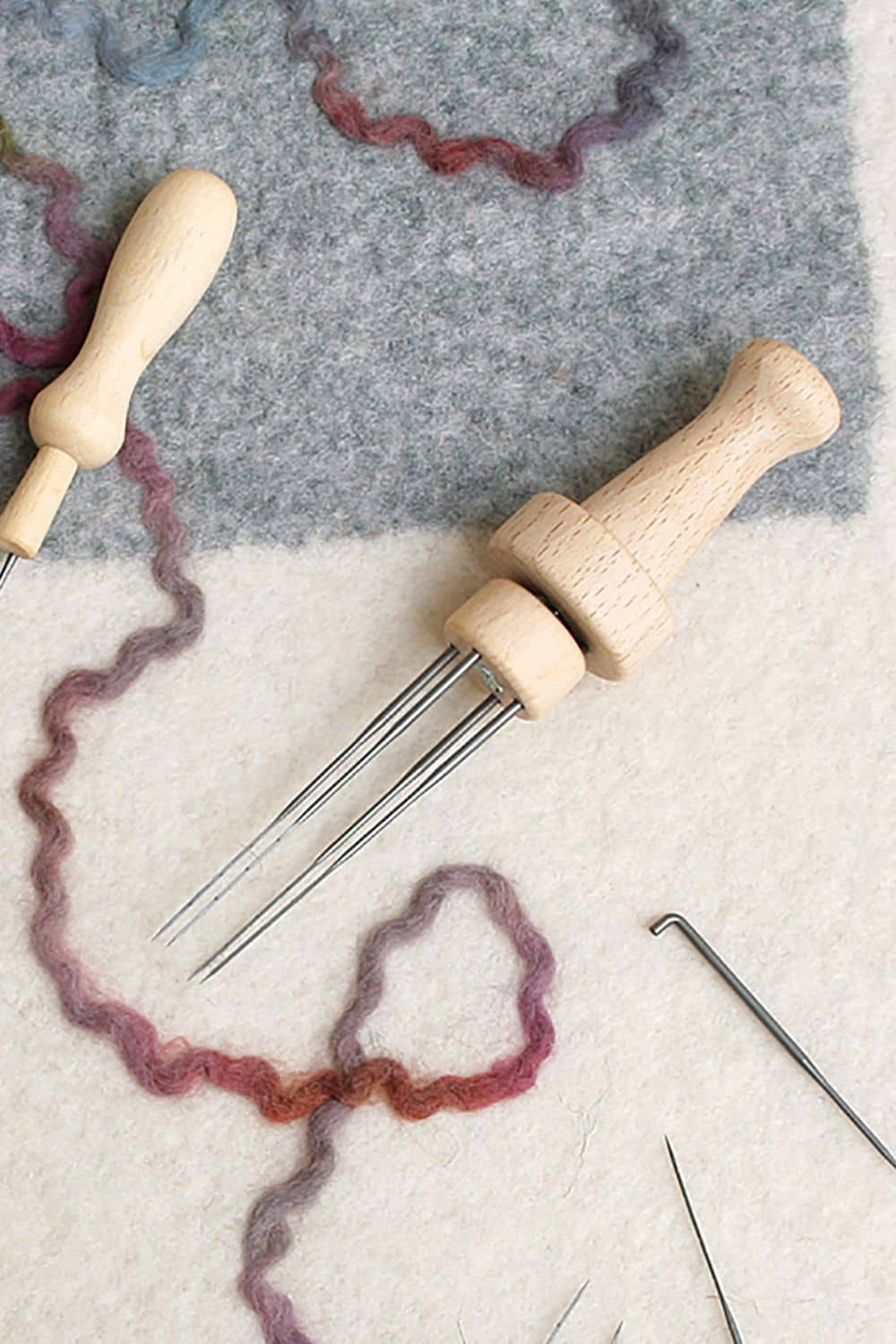 Filznadelhalter für 4 Nadeln Filznadelhalter für vier Nadeln mit Holzgriff auf grau gemustertem Untergrund mit weiteren Nadeln rundherum