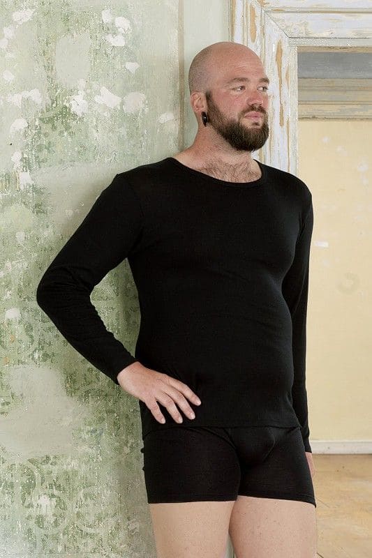 Wolle-Seide Pants Herren Mann trägt schwarze Wolle Seide Pants aus bio Wolle (kbT) und Seide sowie schwarzes Shirt und lehnt an heller Wand