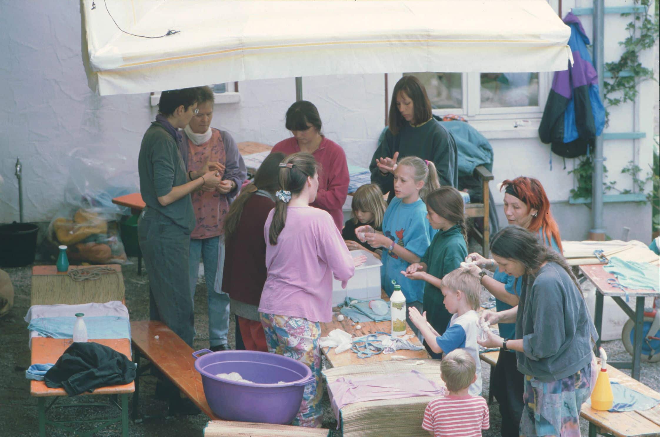 viele Menschen stehen unter einem Schirm um einen Tisch herum und Filzen