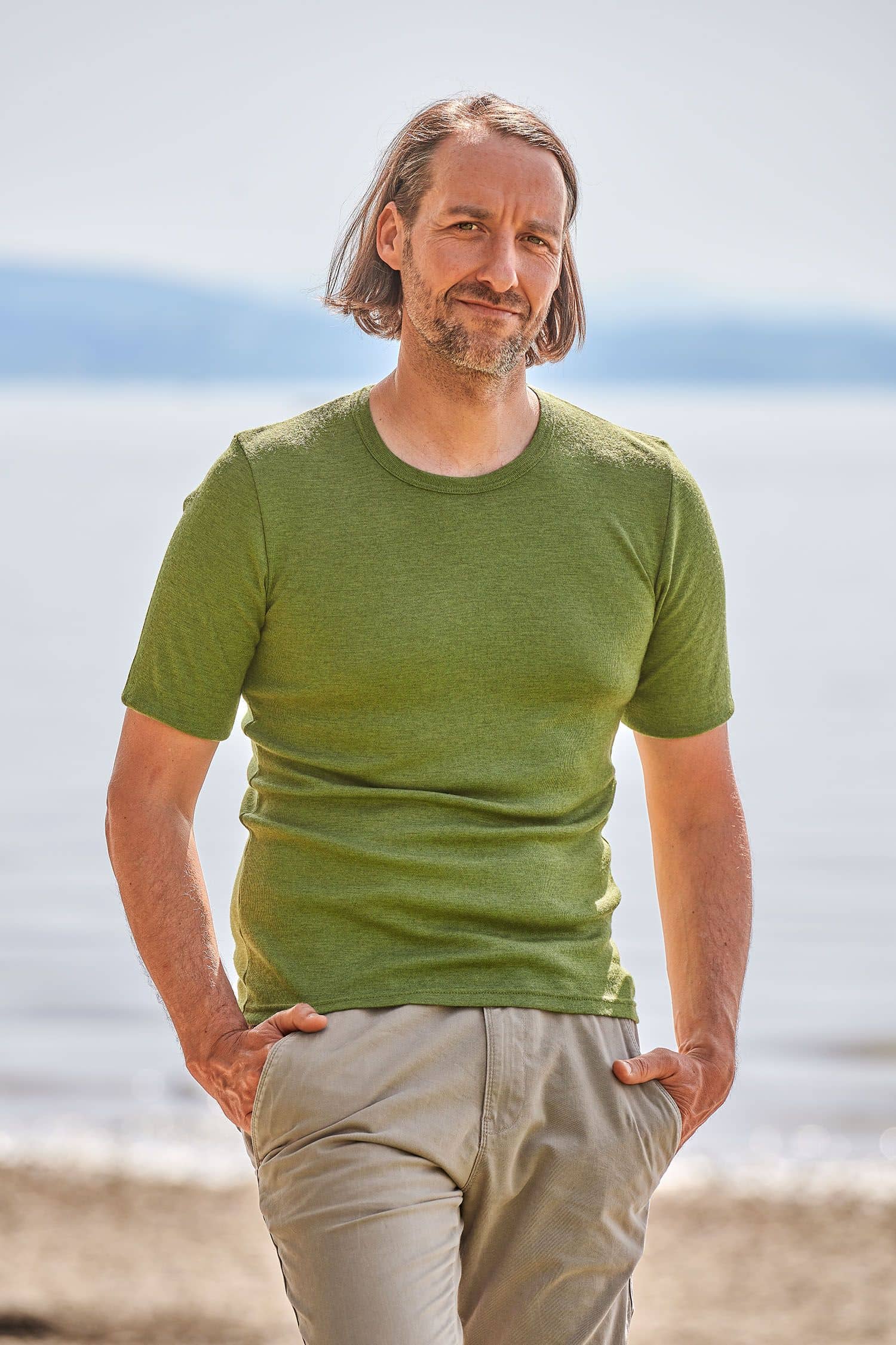 Mann trägt eine beige Hose und ein grünes kurzärmeliges Wollhemd aus bio Merinowolle (kbT)