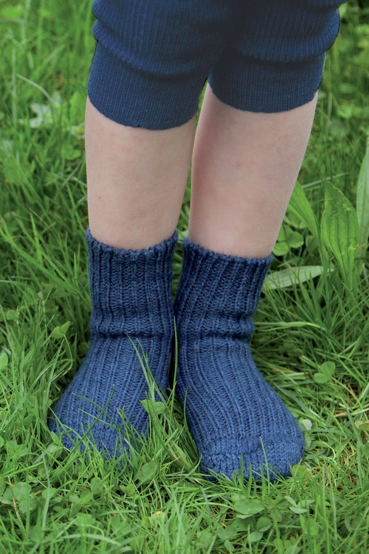 Kind mit marineblauen Wollsocken aus bio Wolle (kbT) steht auf einer Wiese