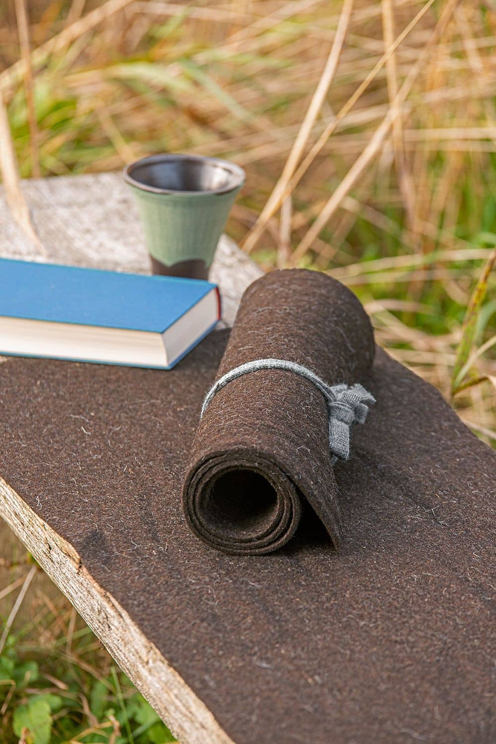 brauner aufgerollter Wollfilz vom Finkhof aus bio Wolle (kbT) auf einer Bank mit Becher und Buch