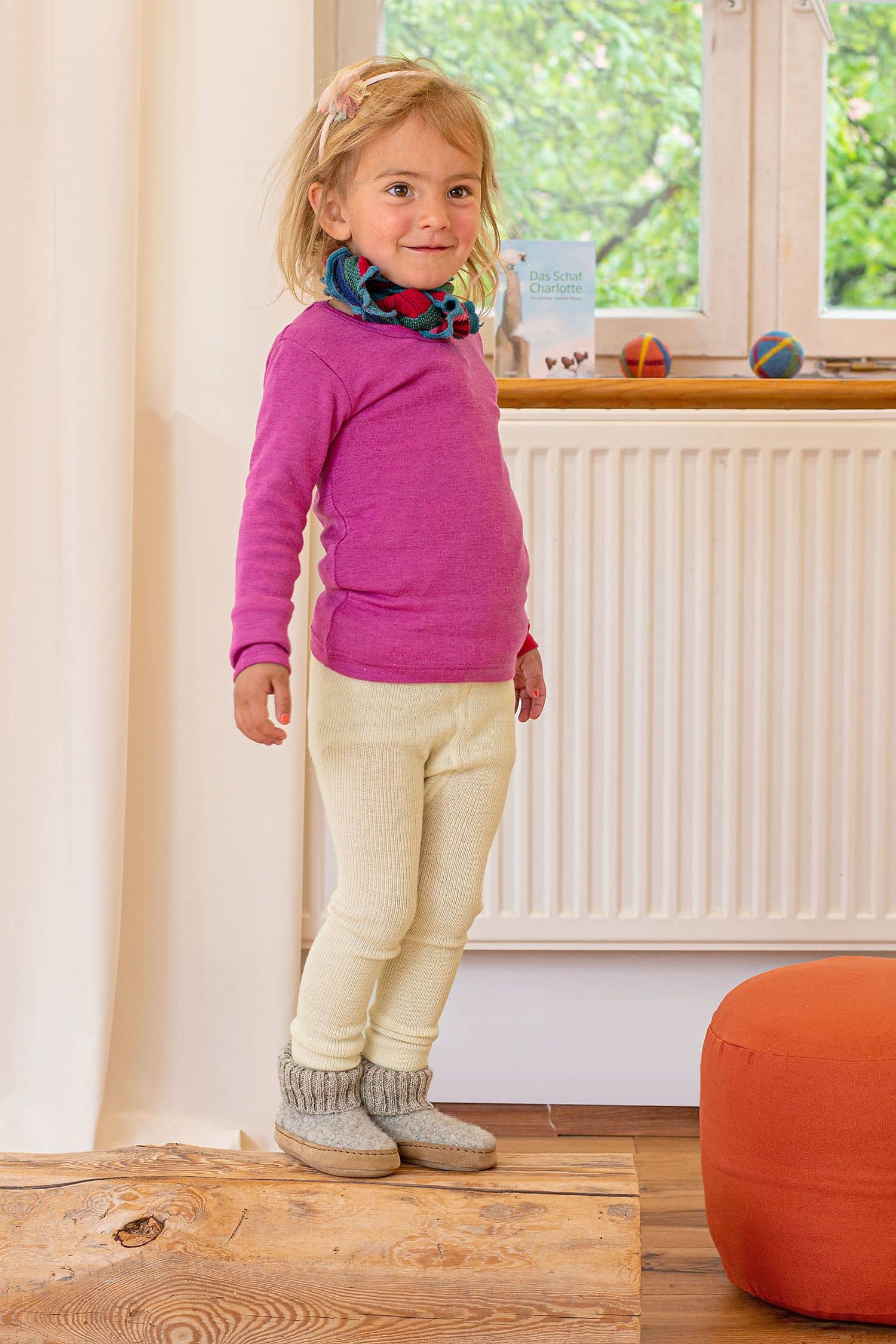 Kind spielt auf Holzstamm mit Wollkleidung und Hüttenschuhen vom Finkhof aus bio Wolle (kbT)