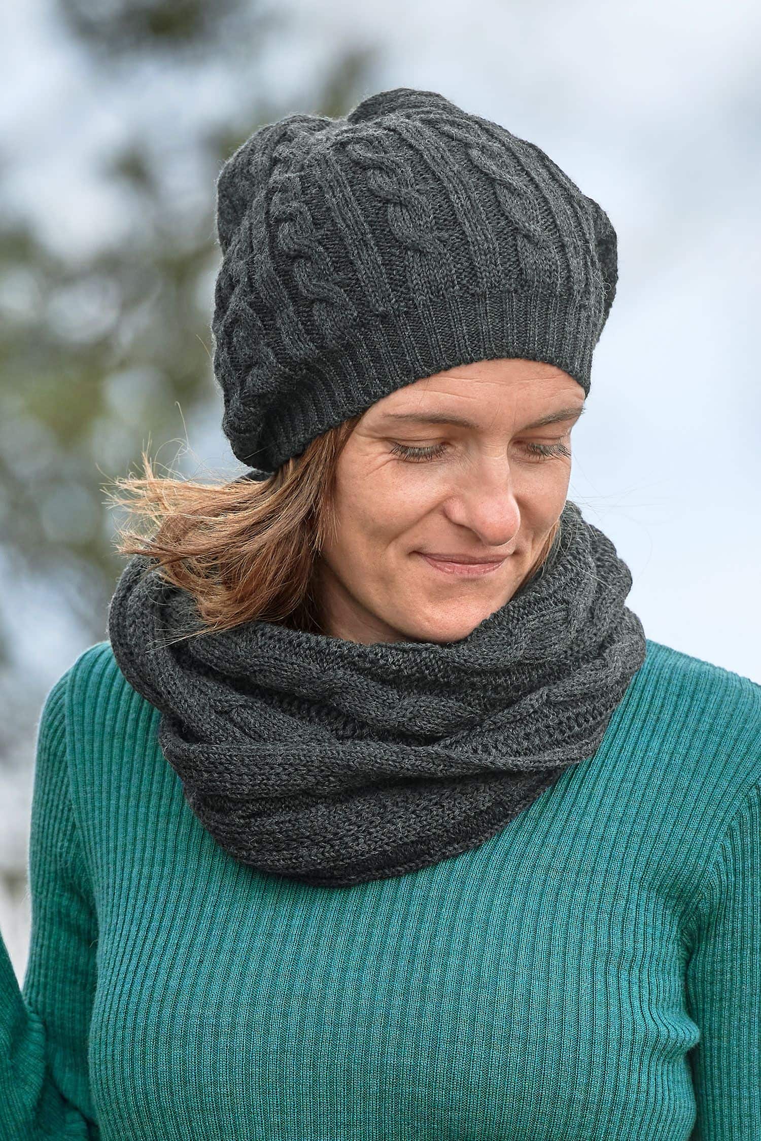 Frau mit türkisem Shirt trägt dunkelgraue Mütze und Loopschal mit Zopfmuster aus bio Wolle (kbT) vom Finkhof