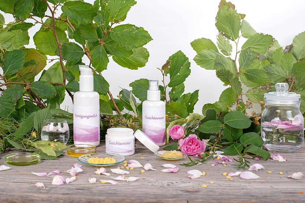 Finkhof Pflegeprodukte auf Stimmungsbild mit Blüten, Tiegeln und Blättern im Hintergrund