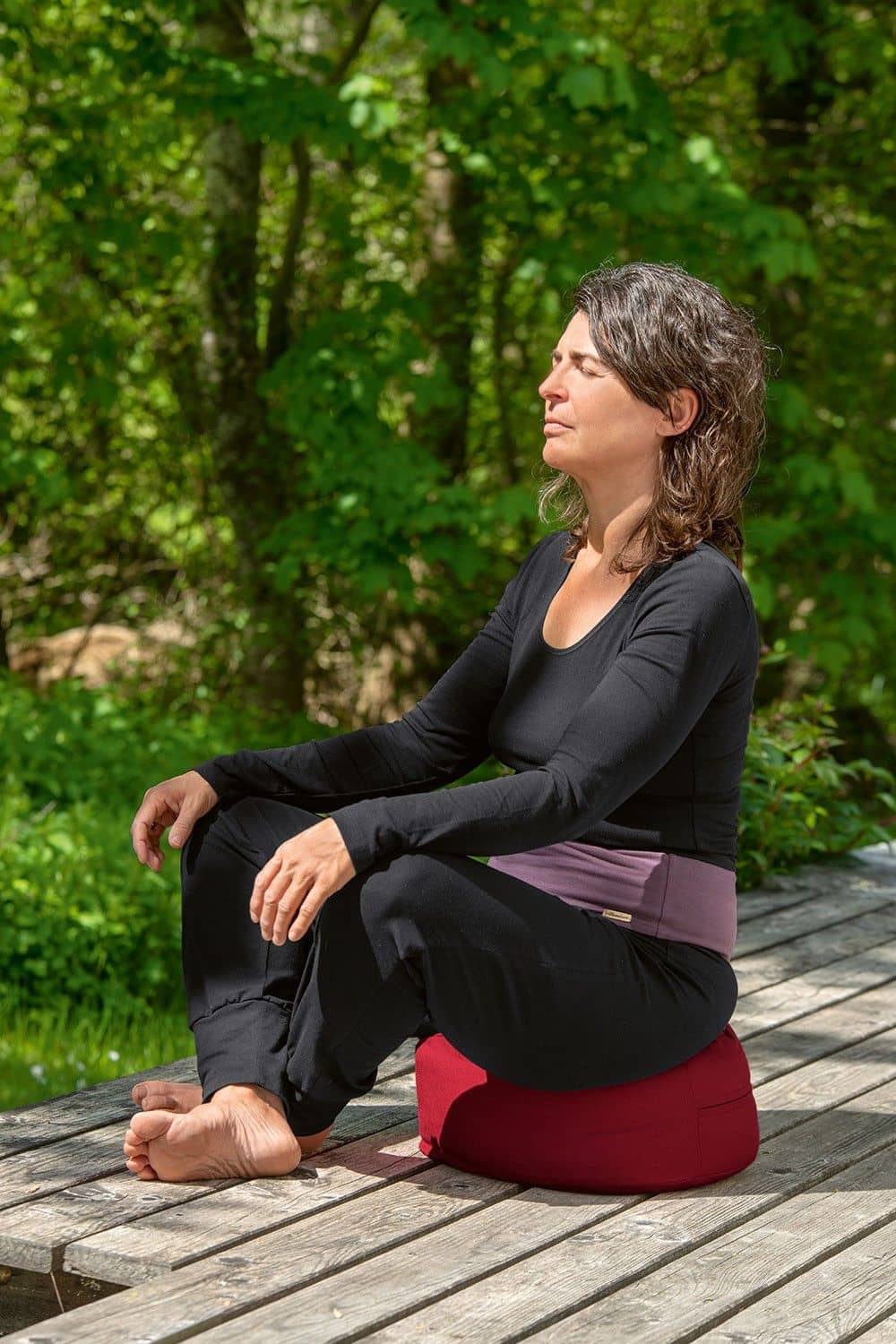 Frau sitzt mit Kissen, Yogahose und schwarzem Langarmshirt aus bio Baumwolle (kbA) und Elasthan auf der Terrasse