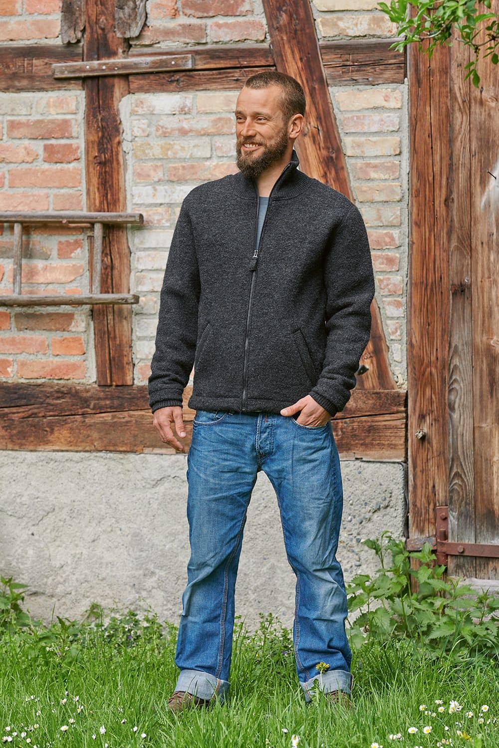 Mann vor alter Wand trägt Finkhof Leichtwalkjacke in anthrazit aus bio Wolle (kbT) mit Stehkragen und Jeans