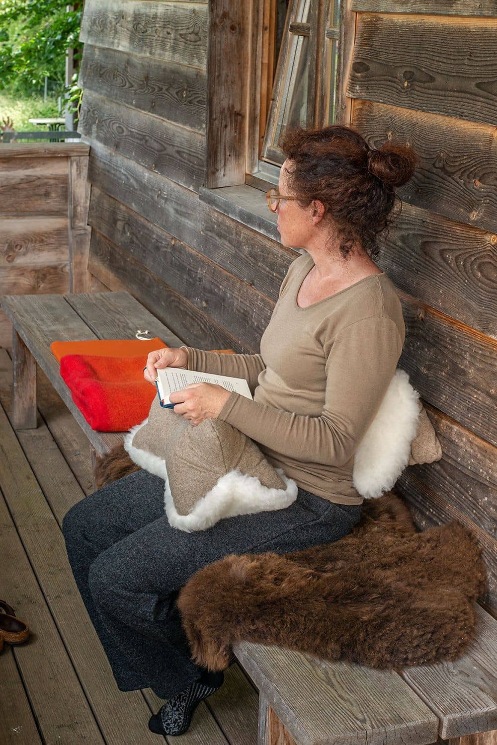 Frau sitzt und liest Buch , welches auf dem Finkhof Leseknochen aus Schaffell, Loden und Rohwolle (kbT) liegt