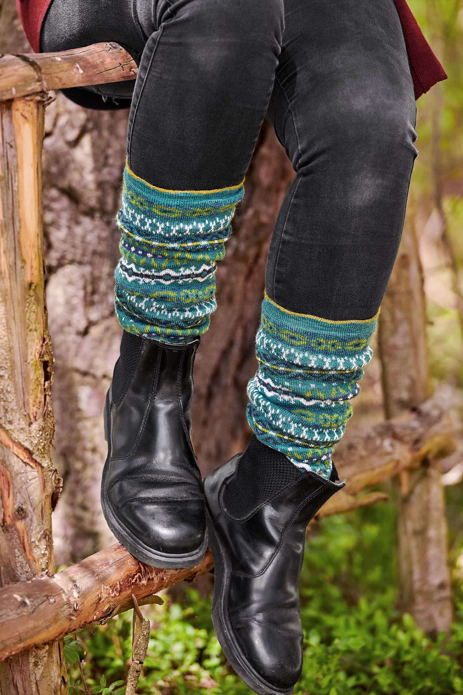 Person sitzt auf Leiter und trägt schwarze Stiefel, Jeans und türkise Beinstulpen mit nordischem Muster aus bio Wolle (kbT)
