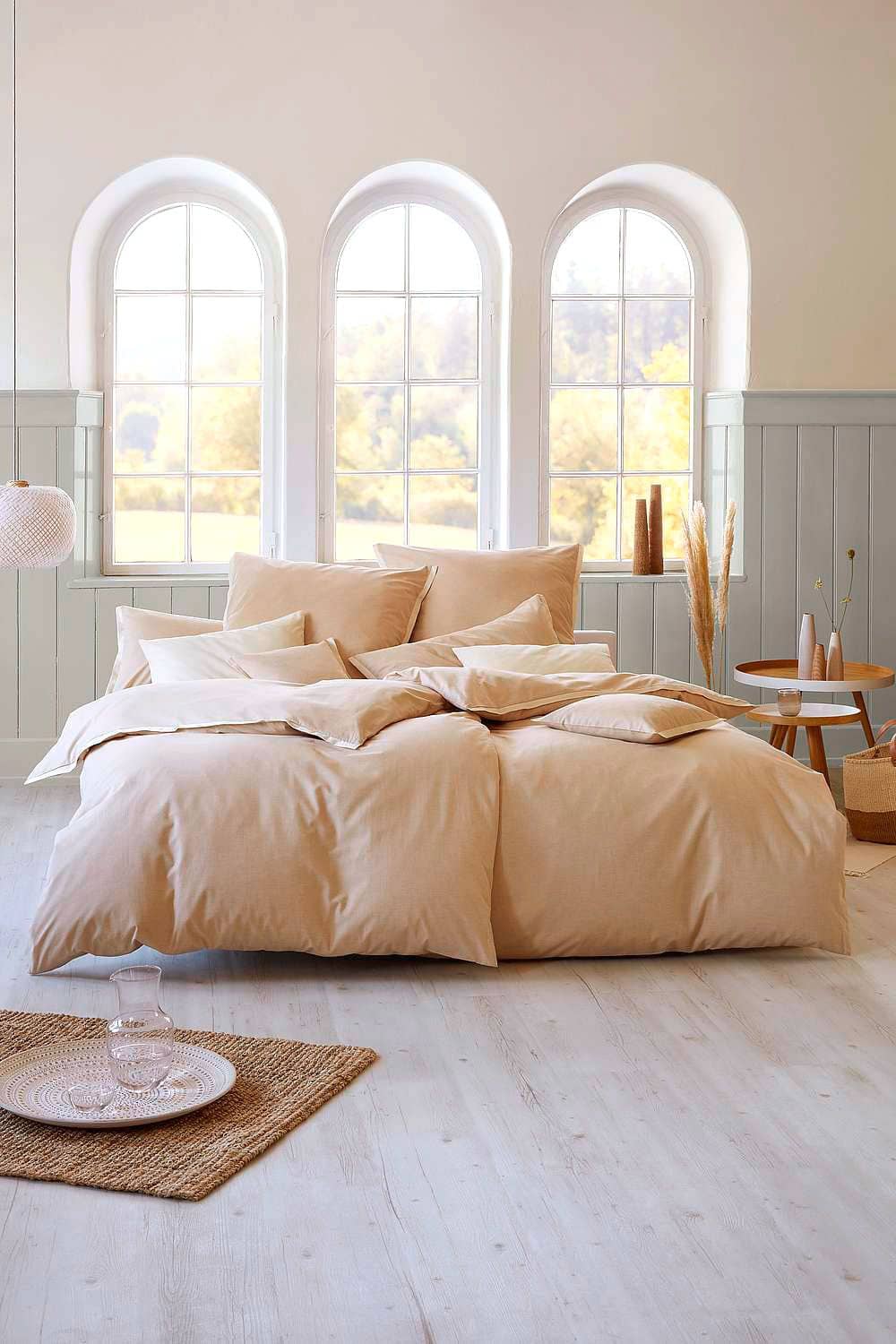 ungefärbte Bettwäsche aus bio Baumwolle (kbA) auf Bett in hellem Zimmer mit großen Fenster, Holzpaneelen und Deko