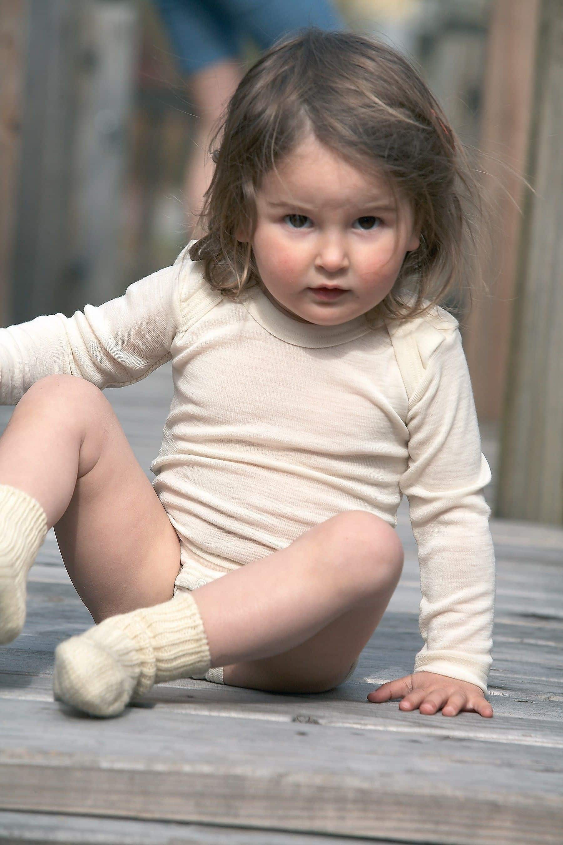 Woll-Body Langarm naturweiß Mädchen trägt naturweißen Woll Langarmbody aus bio Wolle (kbT) und helle Stricksocken