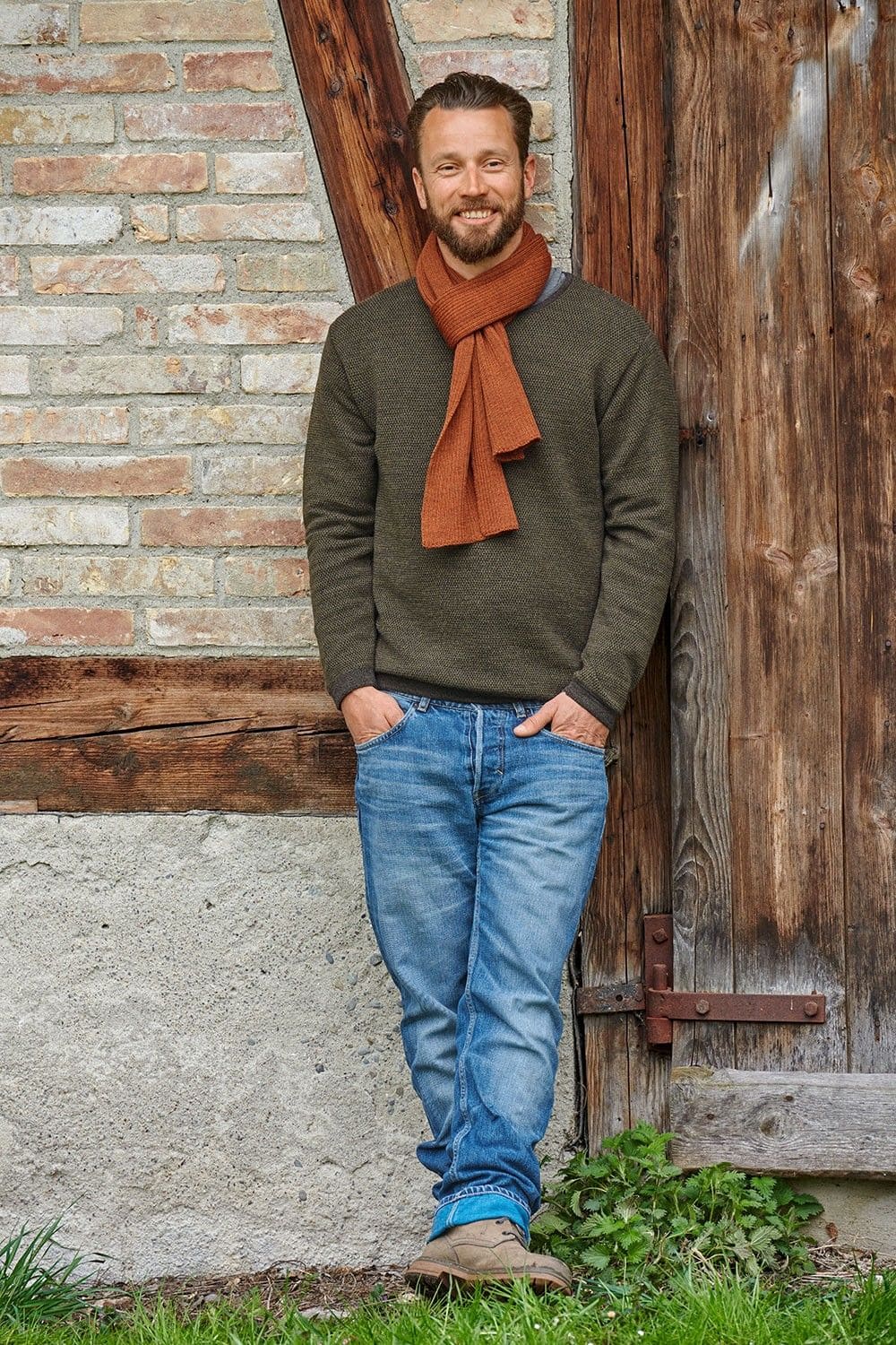 Mann mit grünem Pulli trägt orangen Strickschal aus bio Wolle (kbT) vom Finkhof