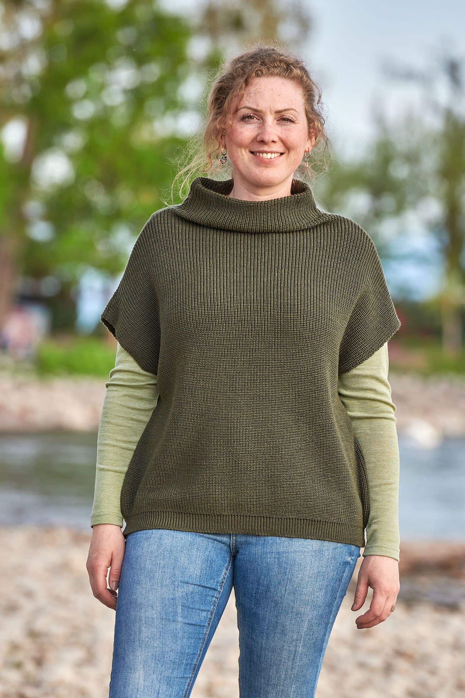 Frau trägt olivegrünen Strickpullunder aus bio Wolle (kbT) vom Finkhof mit grünem Shirt und Jeans