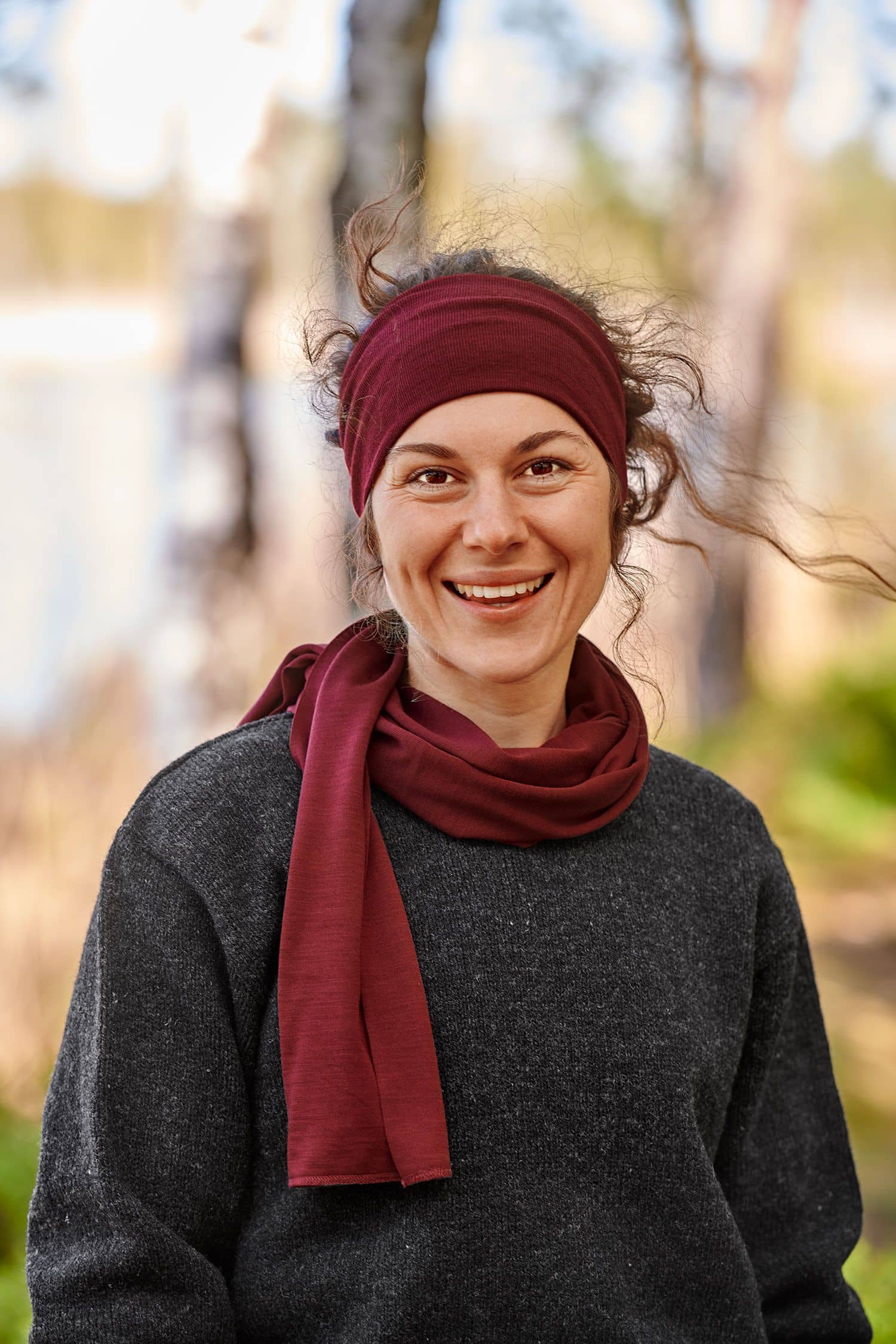 lachende Frau mit grauem Pulli trägt ein bordeauxrotes Stirnband aus bio Wolle (kbT) und Seide mit passendem Schal