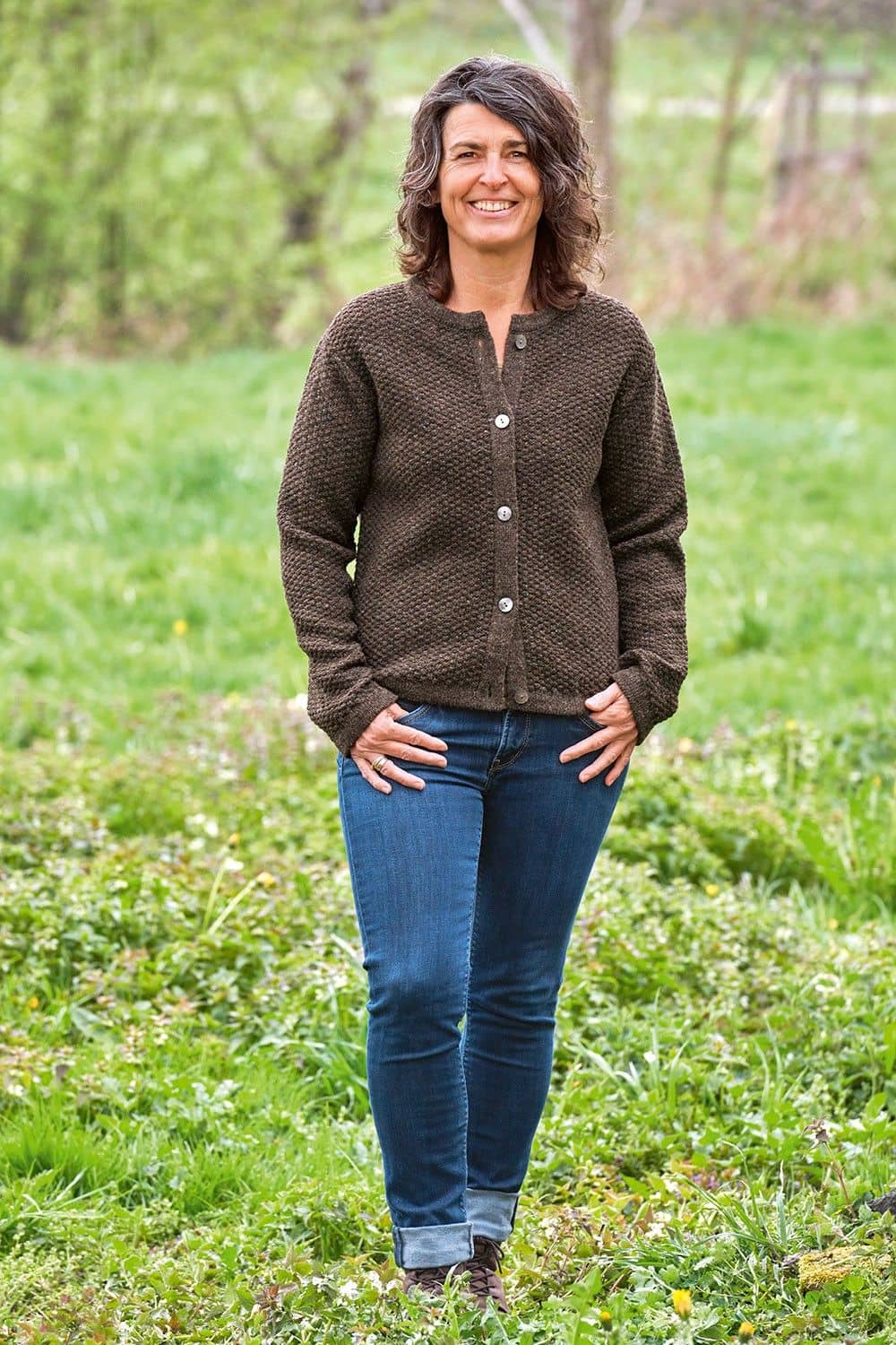 Frau steht auf Wiese und trägt Jeans mit geschlossener brauner Strukturjacke vom Finkhof aus bio Wolle (kbT)
