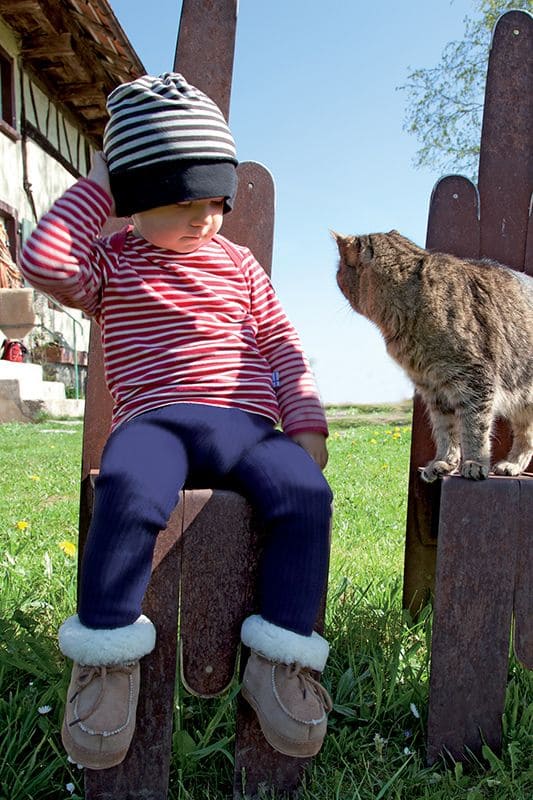 Fellschuhe in braun und weiß aus pflanzlich gegerbtem Schaffell, am sitzenden Kind auf der Wiese mit Katze