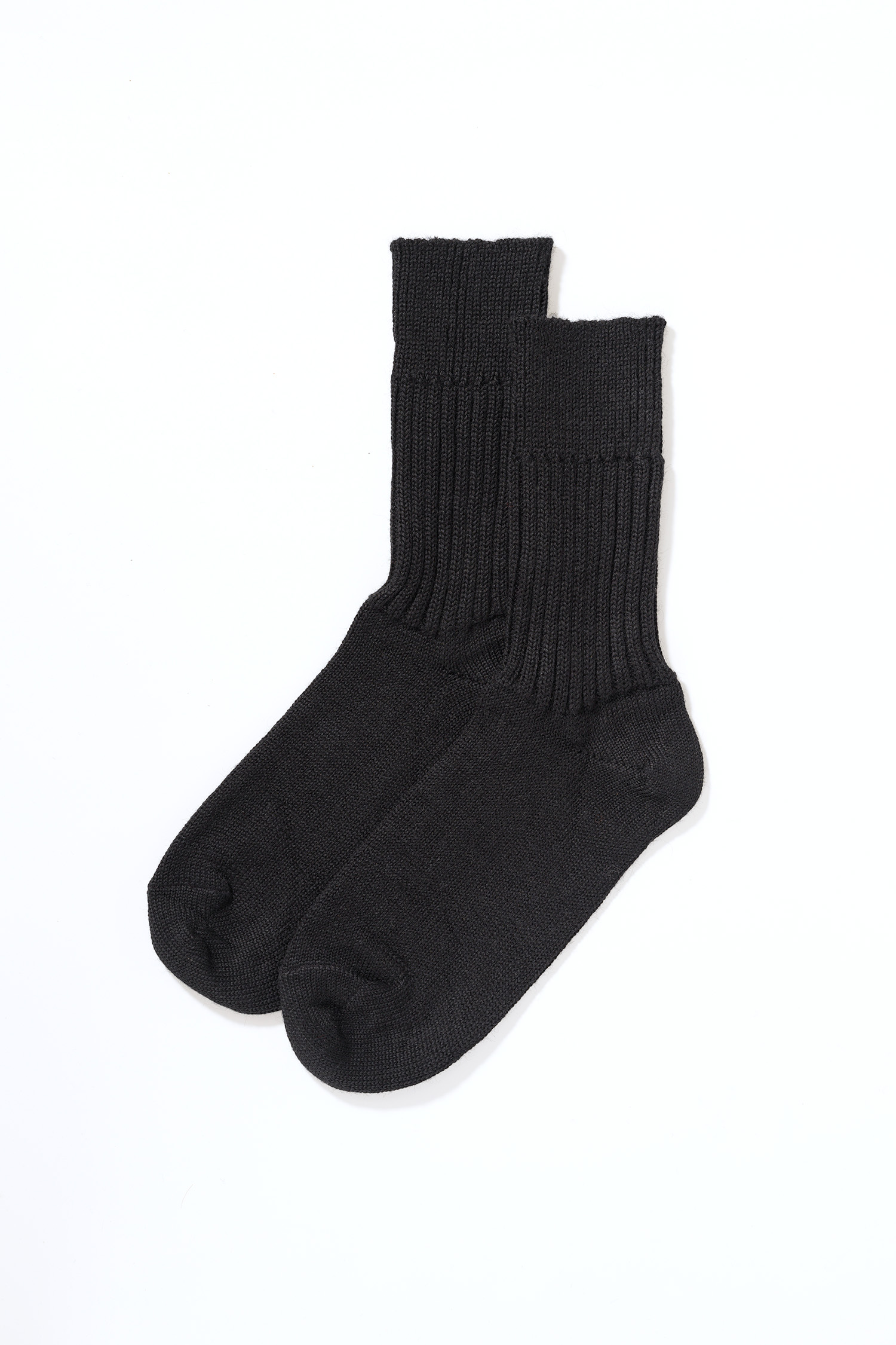 Person steht mit schwarzen Wollsocken aus bio Wolle (kbT) in mittlerer Dicke auf einem Holzboden