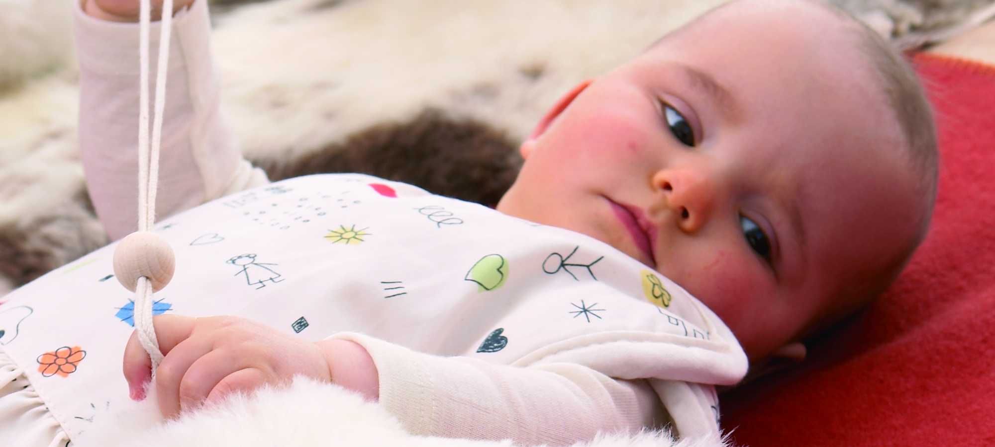 Kind mit Strampler liegt auf roter Decke