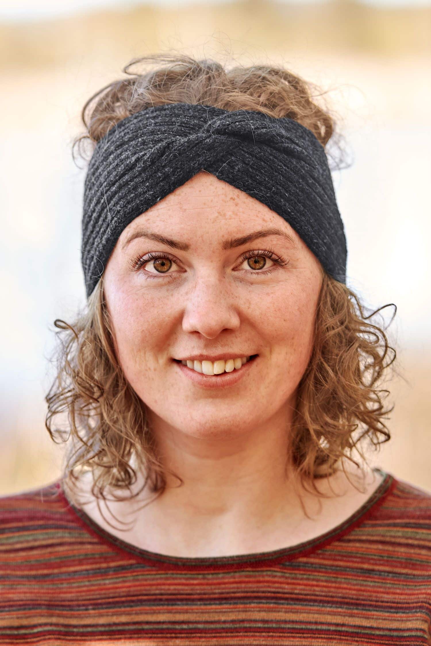 Frau mit orangemeliertem Shirt trägt ein anthrazitgraues Twist Stirnband aus bio Wolle (kbT) vom Finkhof