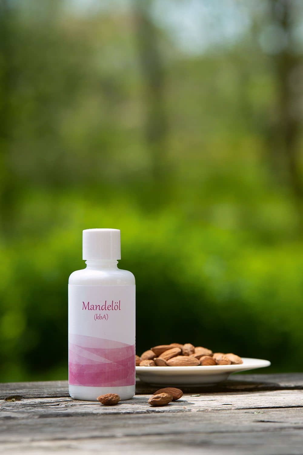Finkhof Mandelöl in weißem 100ml Behälter mit bio Mandeln (kbA), die daneben auf einem Tellerchen liegen