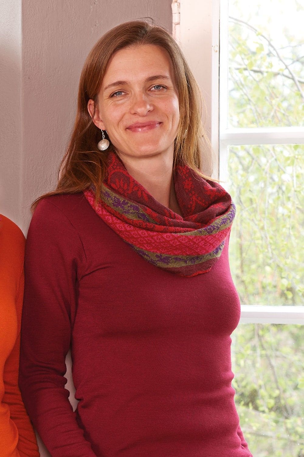 Frau auf Wiese trägt rotes Shirt und Nordic Cacheur mit rotem Loopschal und nordic Muster aus bio Wolle (kbT)