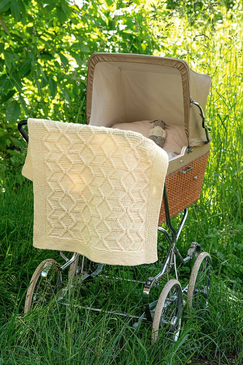naturweiße Decke mit Zopfmuster hängt über Kinderwagen als Strickbeispiele für das Buch ,,Die schönsten Zopfmuster"