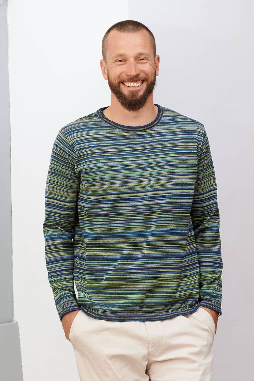 lachender Mann lehnt an Wand und trägt blau grün gestreiftes Shirt aus bio Wolle (kbT) vom Finkhof