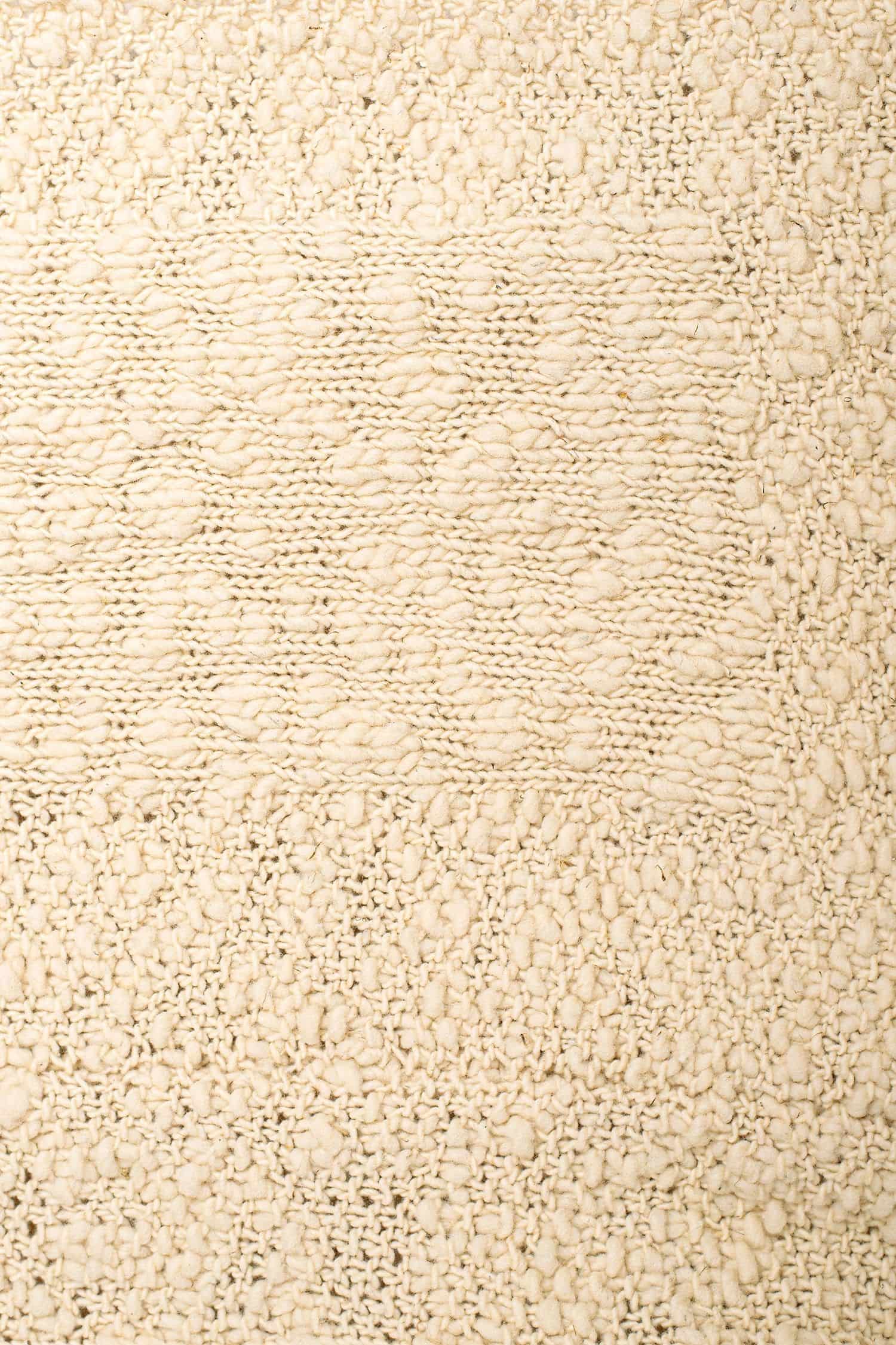 Nahaufnahme der Struktur der naturweißen Decke mit roten Details aus Flammengarn vom Finkhof aus bio Wolle (kbT)