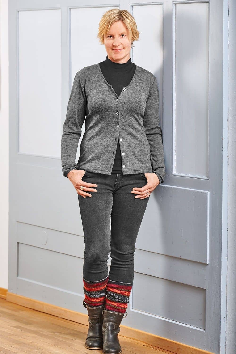 Frau mit schwarzer Hose und Shirt trägt grauen Cardigan und rot grau gemusterte Beinstulpen aus bio Wolle (kbT)