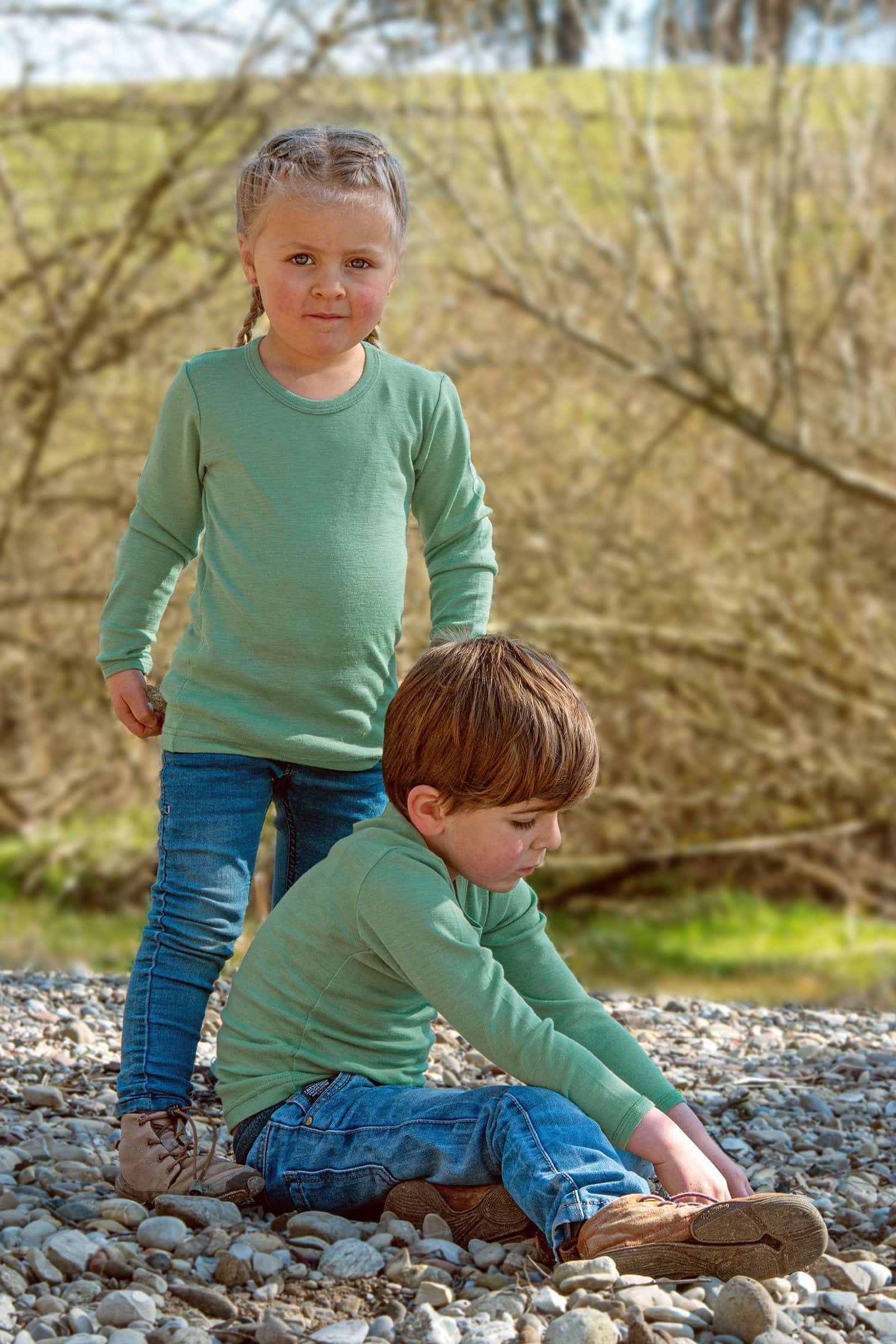 Kinder spielen mit Steinen und tragen schilfgrüne Langarmshirts aus bio Wolle (kbT) und Seide mit Jeanshosen