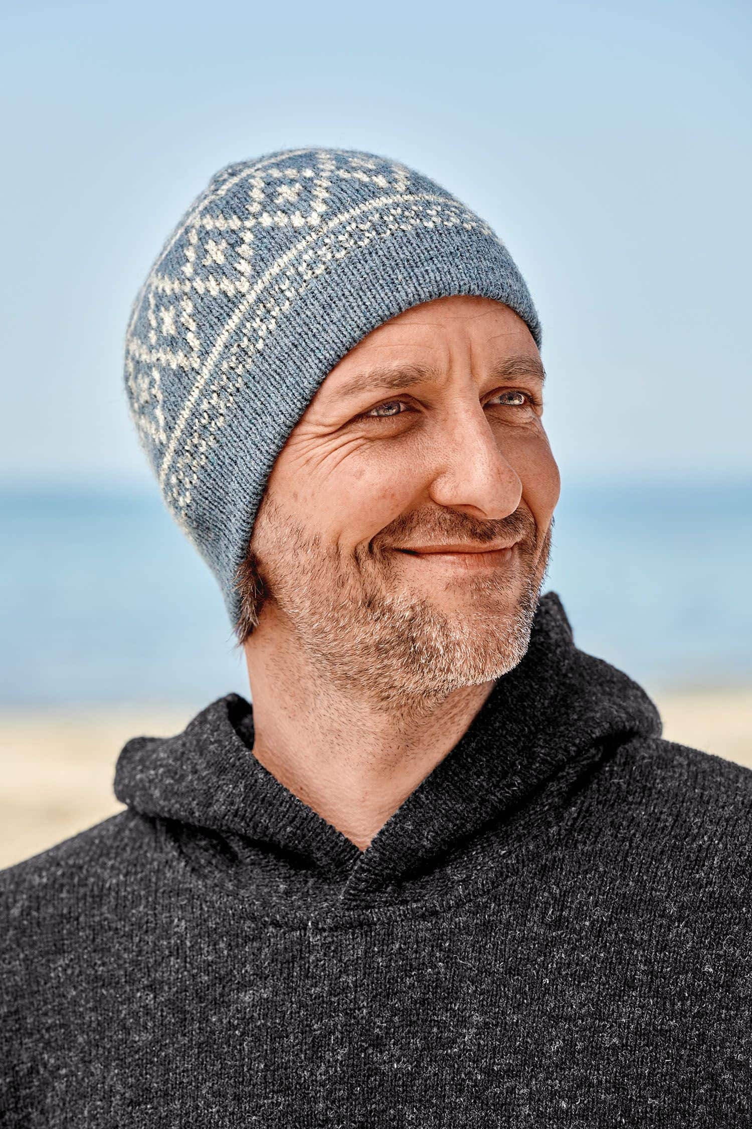 Mann trägt rauchblaue Mütze mit Norwegermuster aus bio Wolle (kbT) vom Finkhof und einen grauen Hoodie