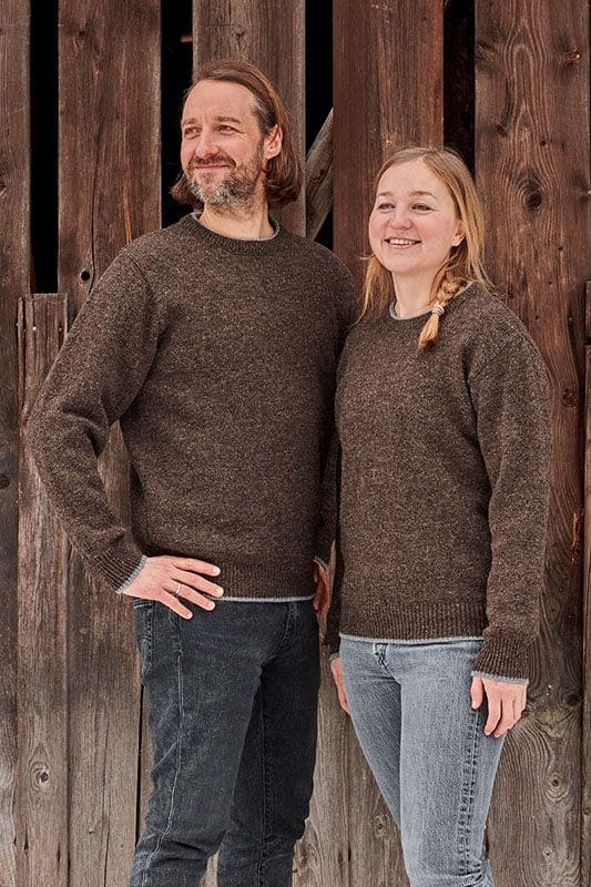 Mann und Frau vor Holzfassade mit braunen Finkhof Pullis aus bio Wolle (kbT)