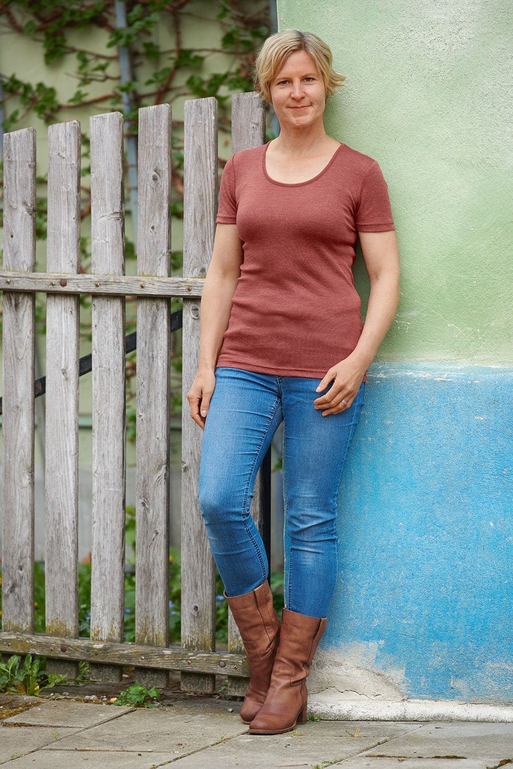 Frau lehnt mit Jeans und rostrotem Kurzarmshirt aus bio Wolle (kbT) und Seide an einer Wand