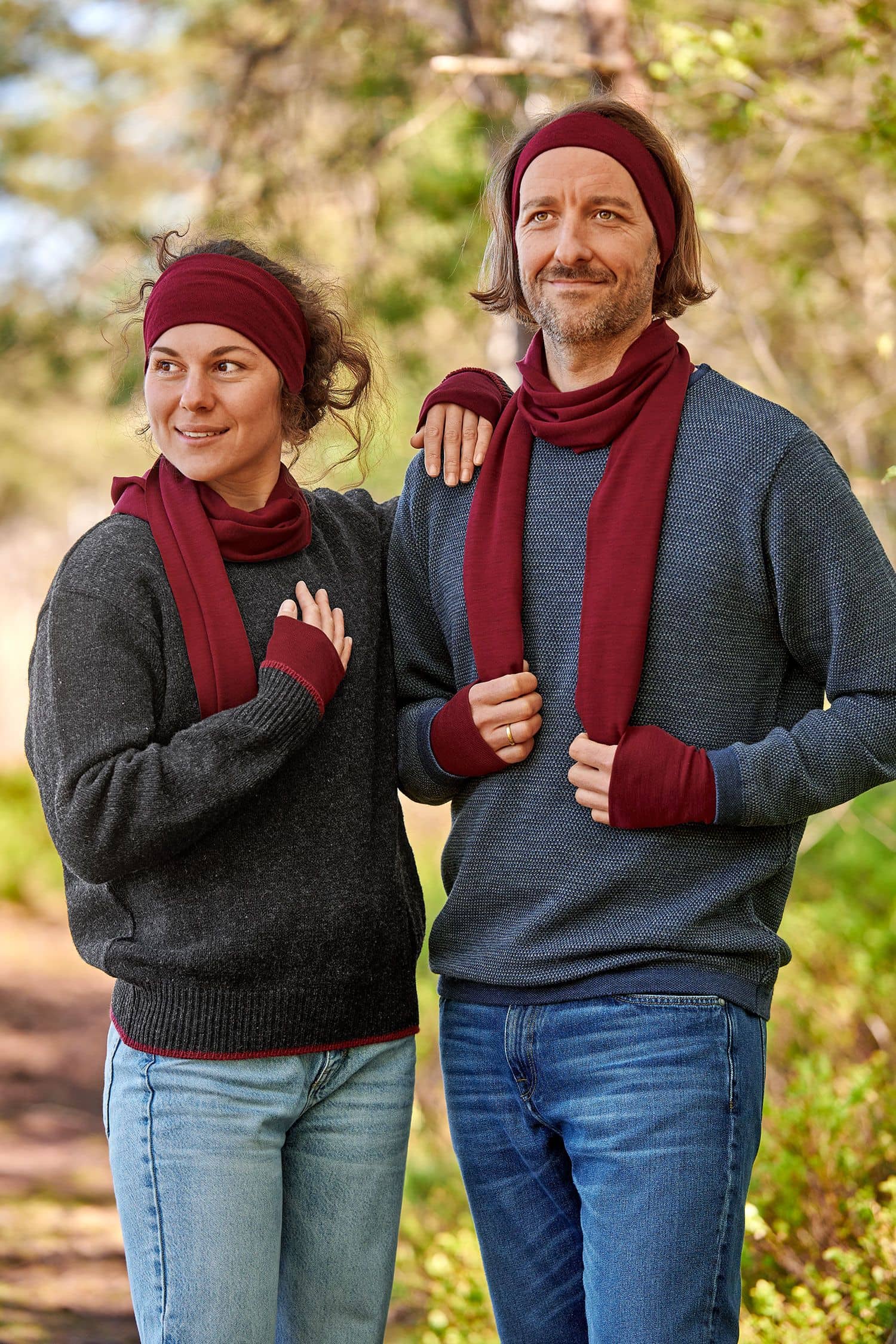 Mann und Frau mit dunklen Pullis tragen bordeauxrote Stirnbänder, Schals und Pulswärmer aus bio Wolle (kbT) und Seide