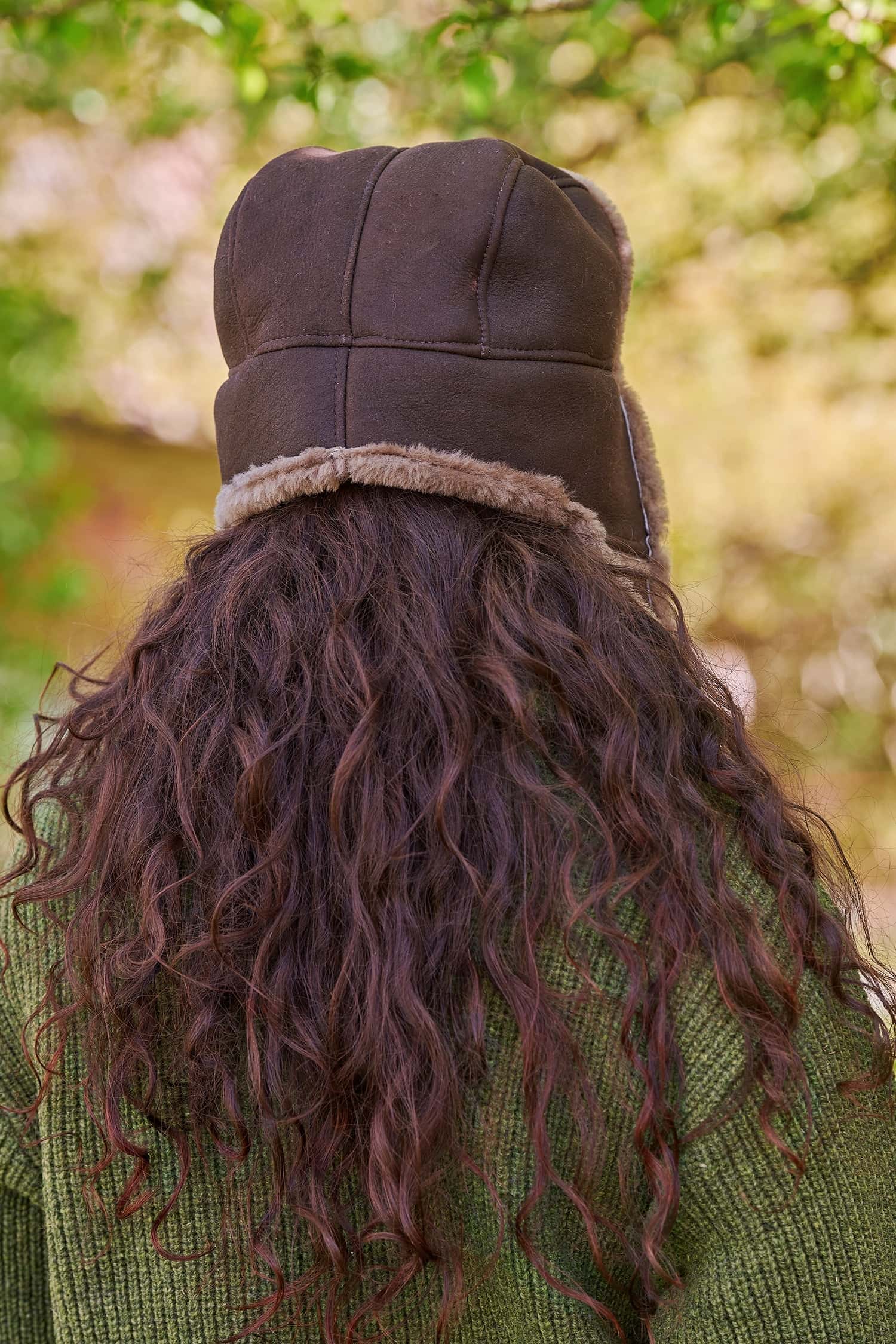 Rückansicht von Frau mit dunklen Locken, die eine braune Finkhof Fellmütze und einen grünen Pullover trägt