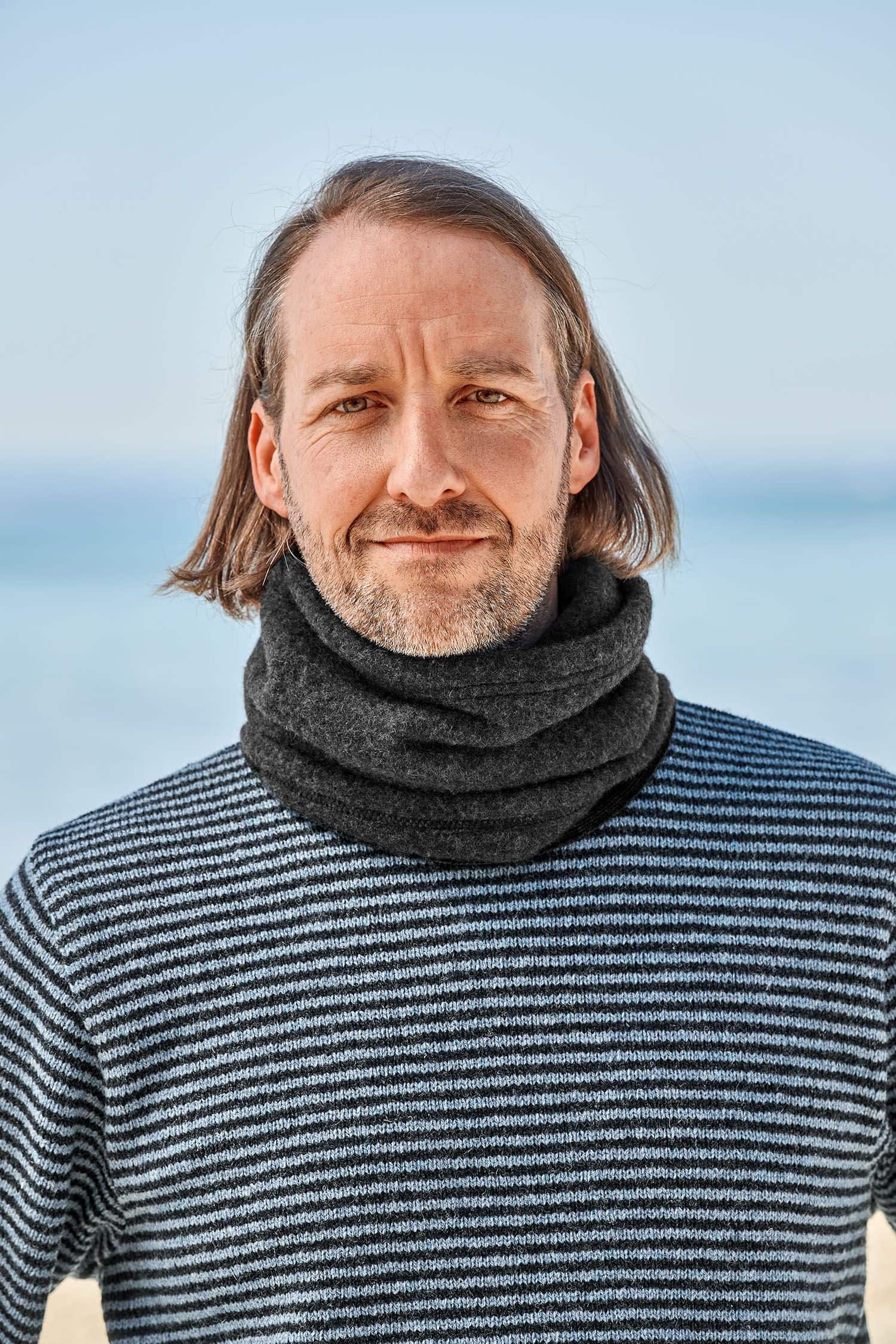Mann mit Streifenpulli trägt dunkelgrauen Schlupfschal aus bio Merinowolle (kbT) vom Finkhof