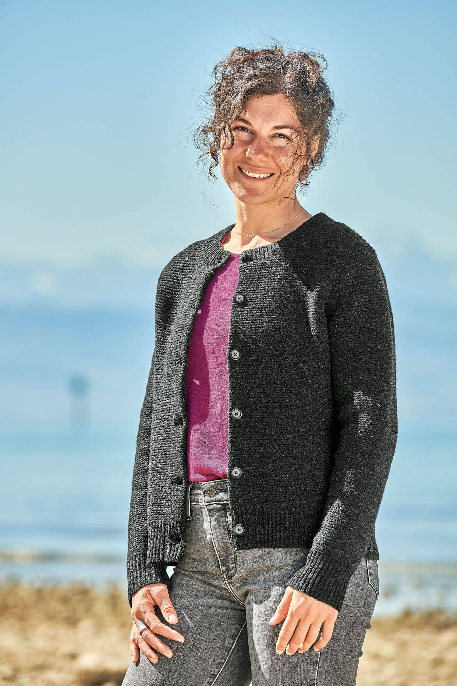 Frau trägt eine graue Jeans, ein lila Shirt und eine dunkelgraue Strickjacke vom Finkhof aus bio Merinowolle (kbT)