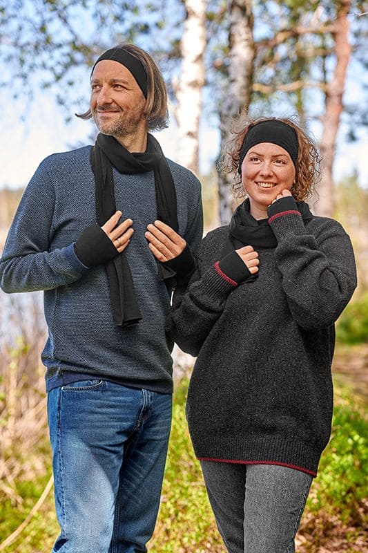 Mann und Frau mit dunklen Pullis tragen schwarze Pulswärmer Stirnbänder und Schals aus bio Wolle (kbT) und Seide